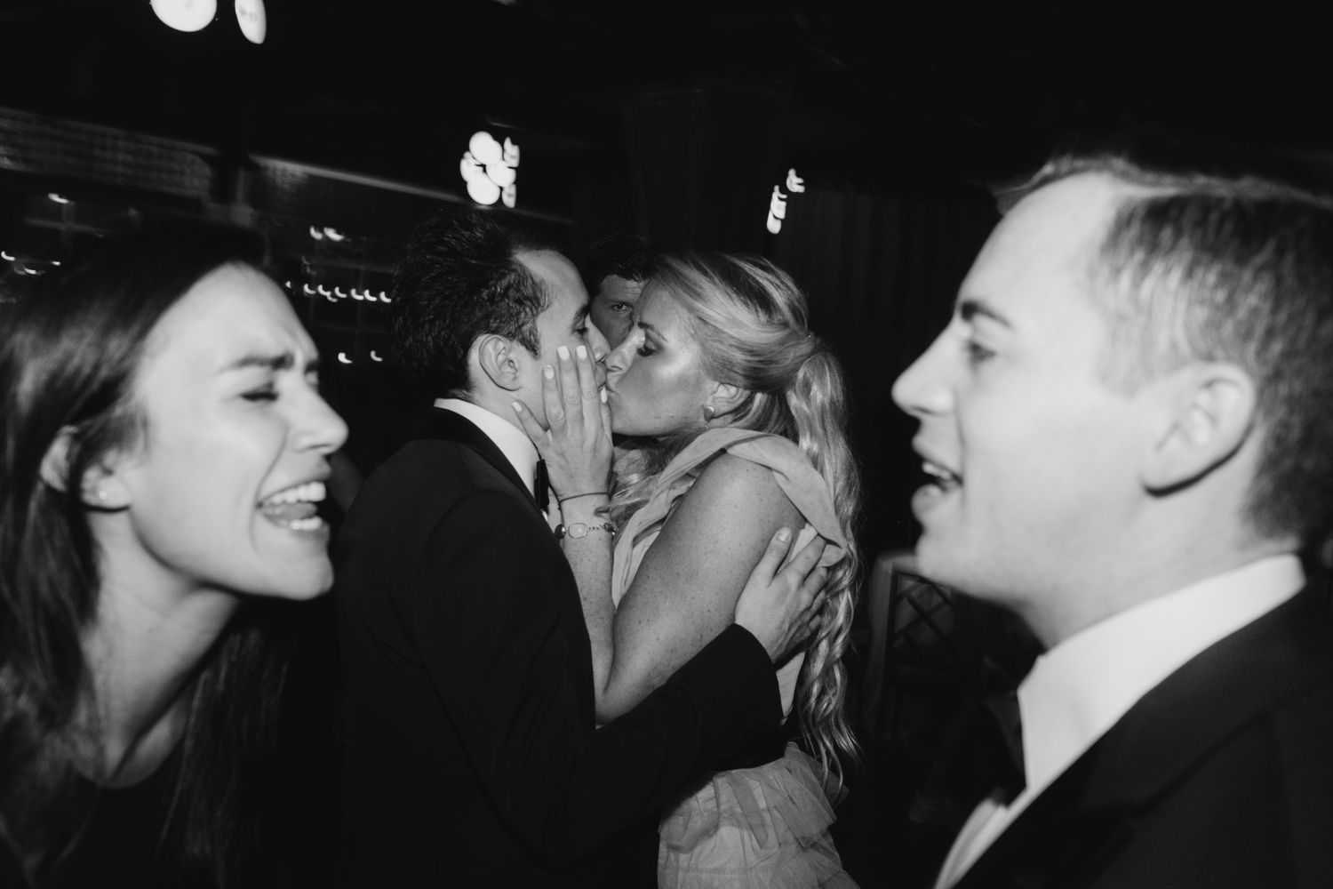 chaotic candid wedding photo of couple yelling at each other while couple kisses in background and man's eye stares