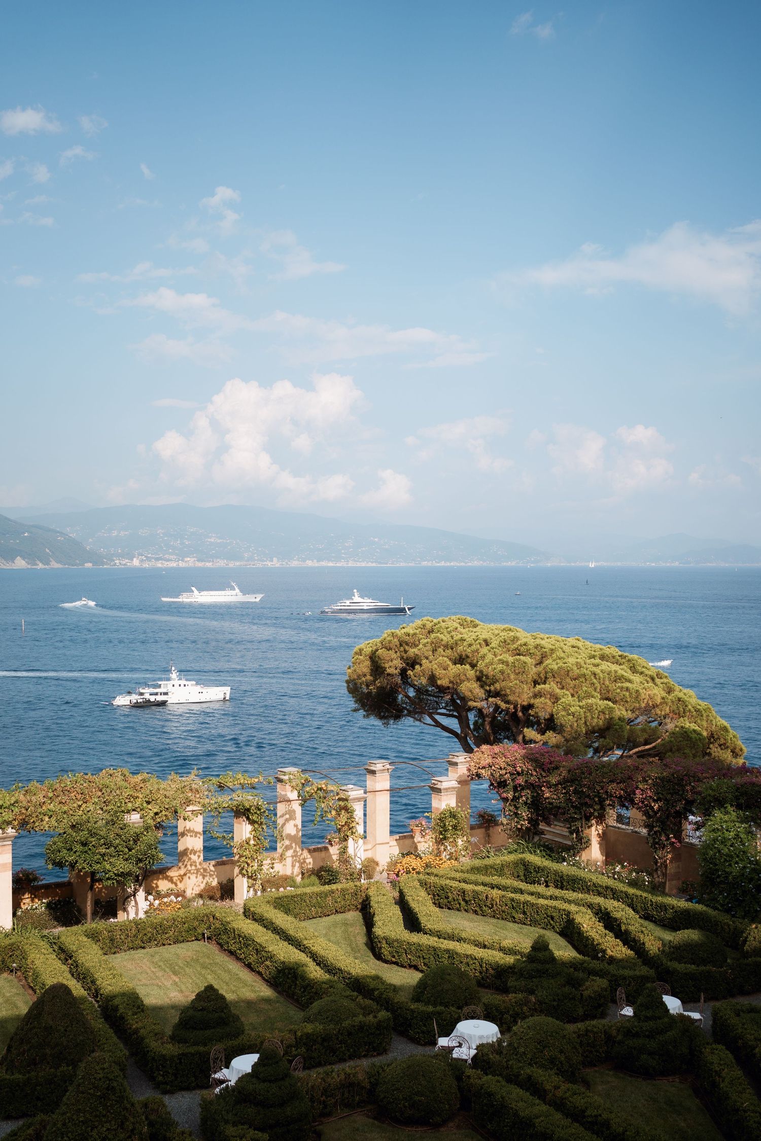 Panoramic view of a Mediterranean garden terrace with luxury yachts in the distance.
