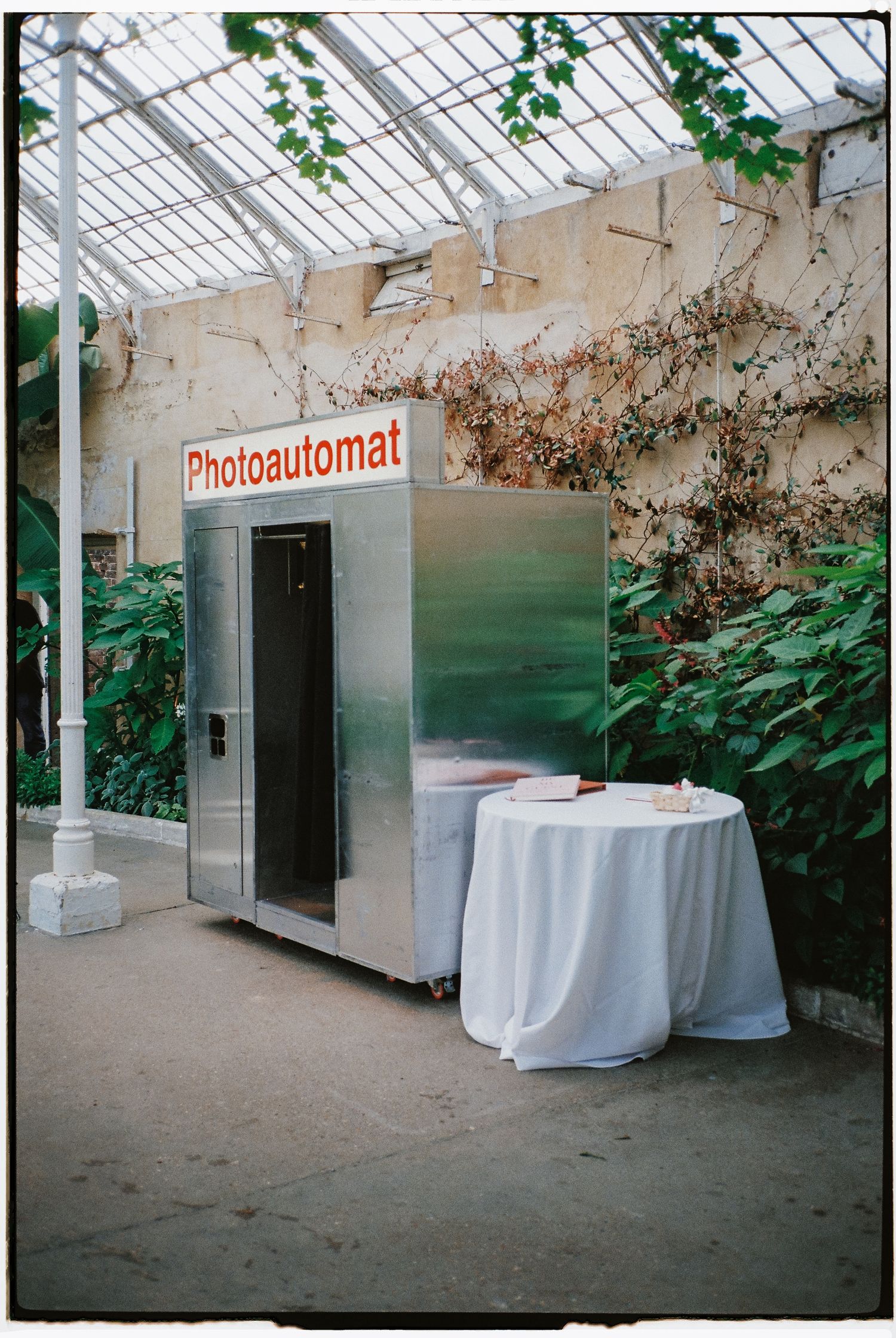 Photo booth setup with white curtains in a greenhouse space with a Photoautomat sign.