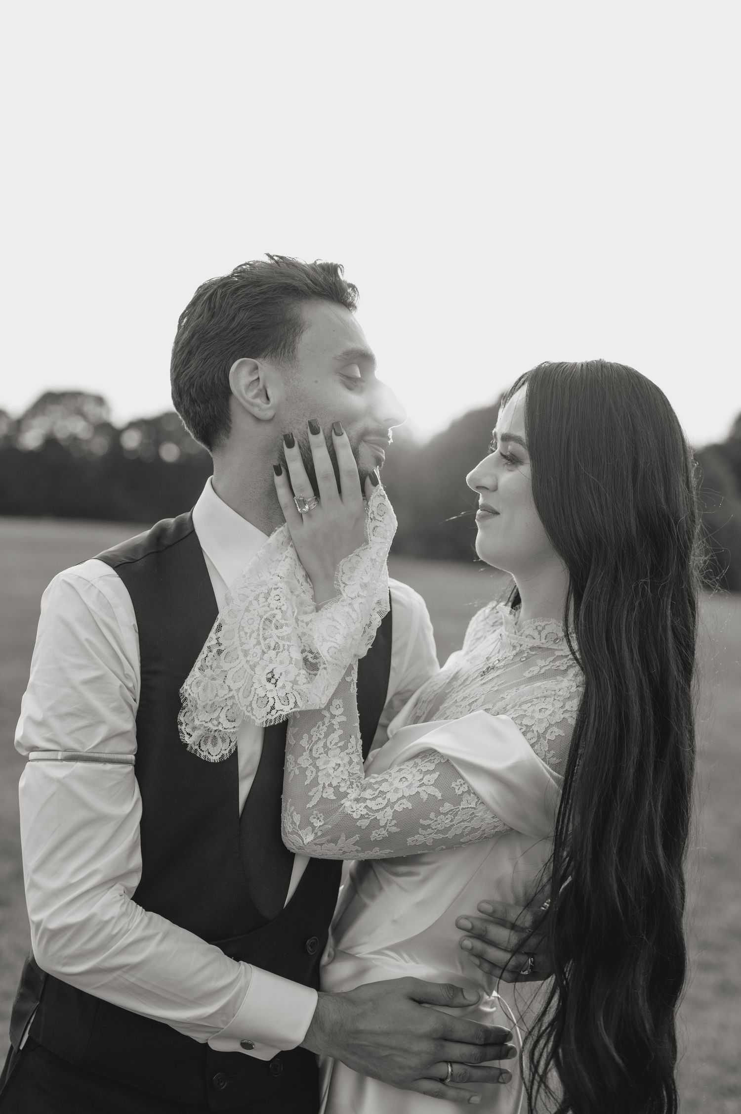 Black and white wedding photo of bride touching groom's face tenderly in an outdoor field setting.