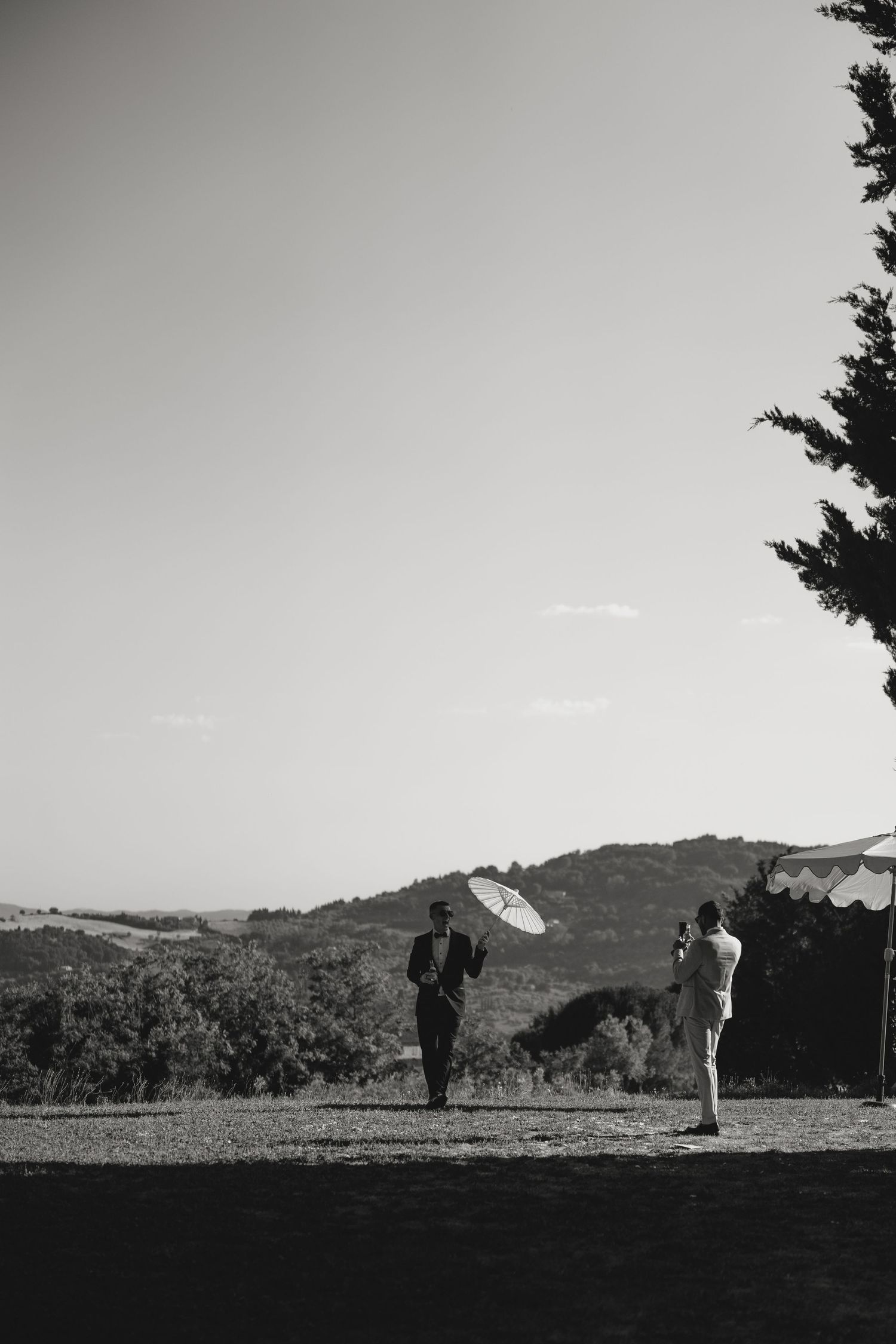 Black and white photo of two people with parasols in a scenic countryside landscape with rolling hills.