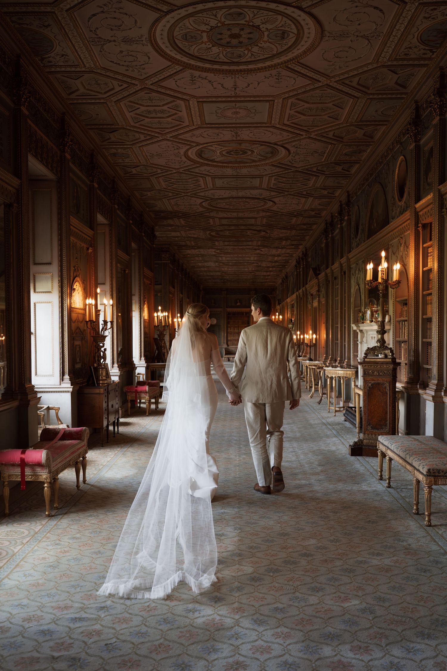 Elegant long hallway with ornate ceiling, chandeliers and wedding dress silhouettes.