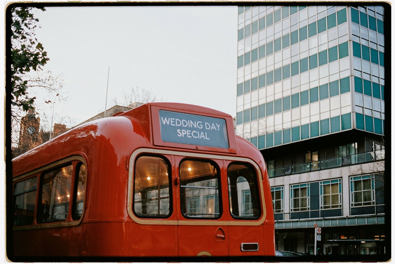 Vintage red double-decker bus with 'Wedding Day' sign parked in front of a modern building.