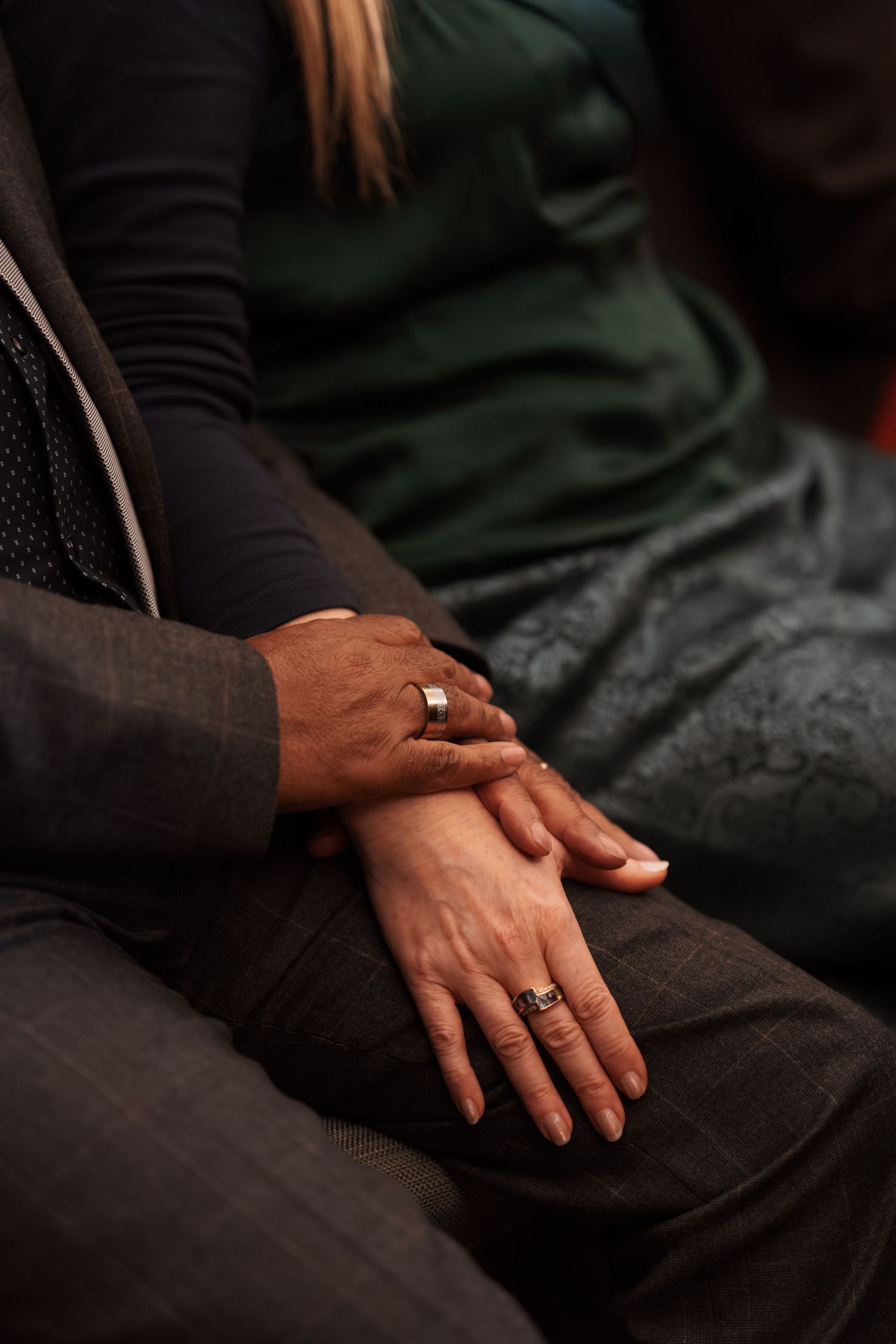 Close-up of hands with wedding rings resting on dark fabric.