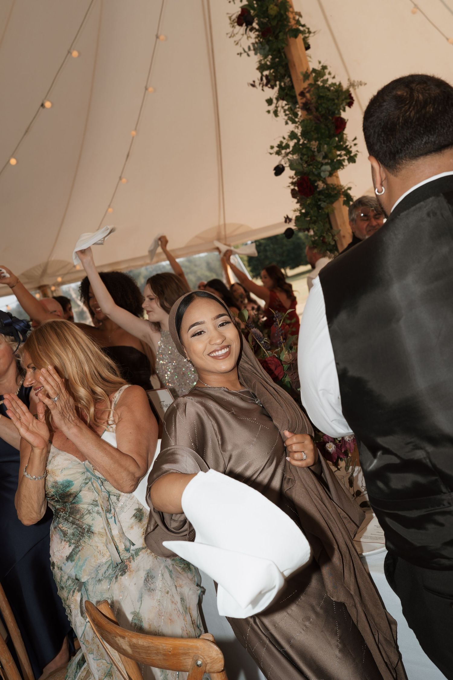 Wedding guests dance and celebrate under a decorated tent with string lights.