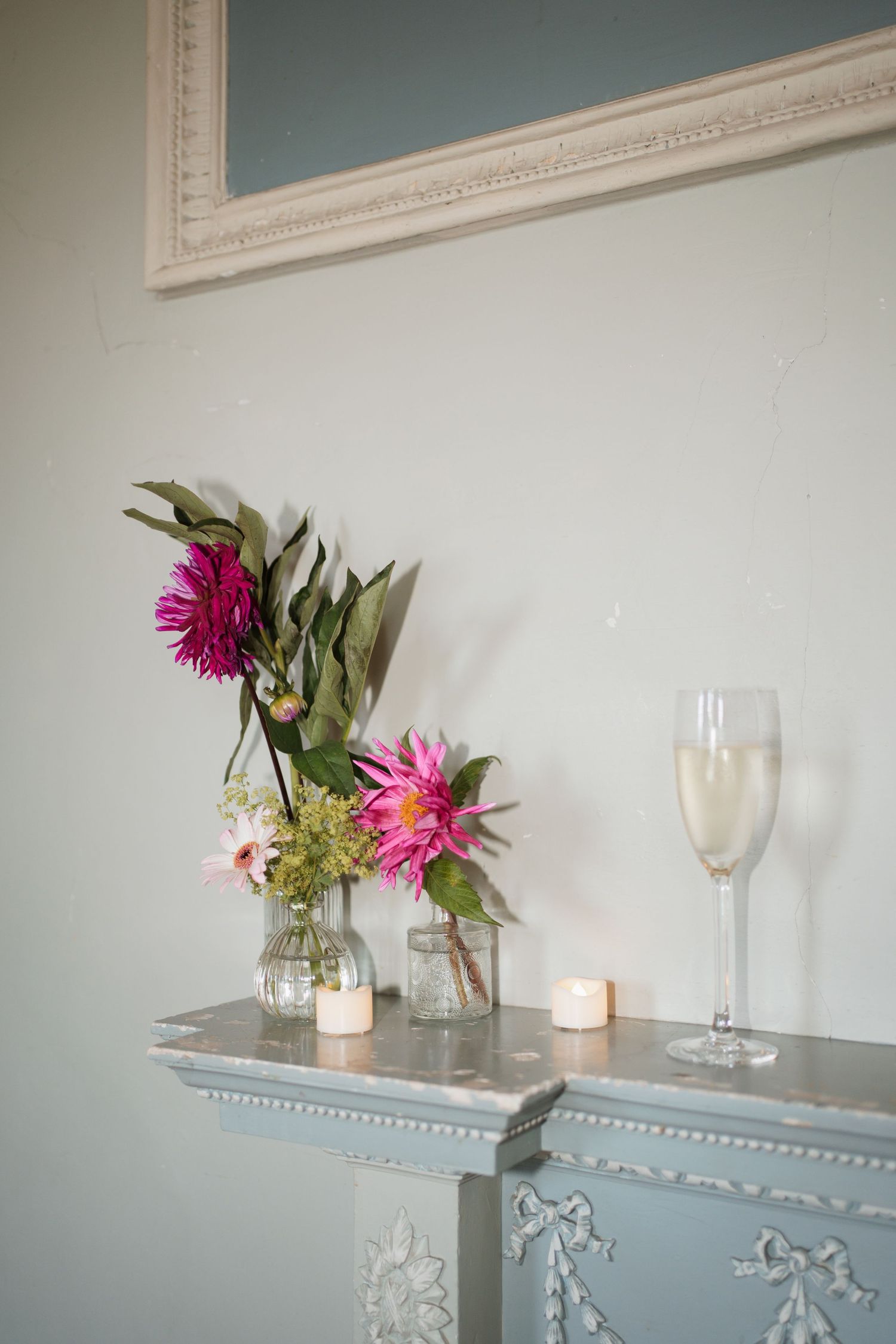 Pink flowers in vase with wine glasses and candles on elegant mantle display.