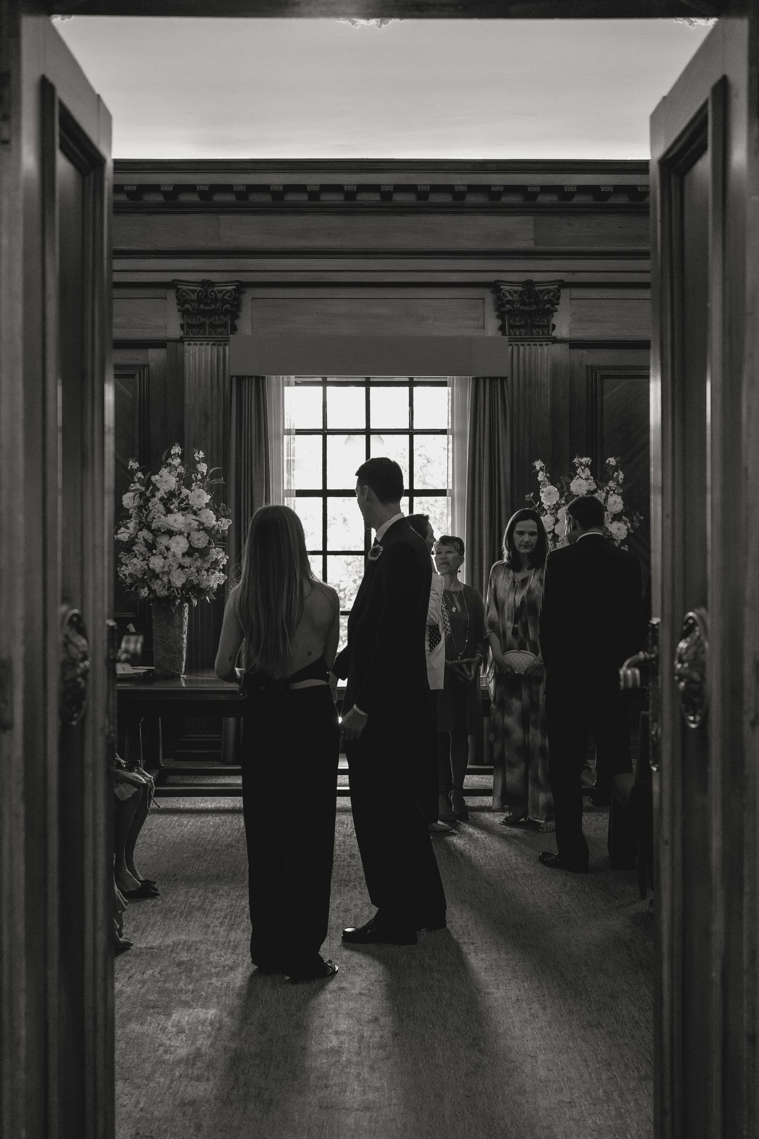 Silhouettes of guests framed by doorway at an elegant venue with floral arrangements.