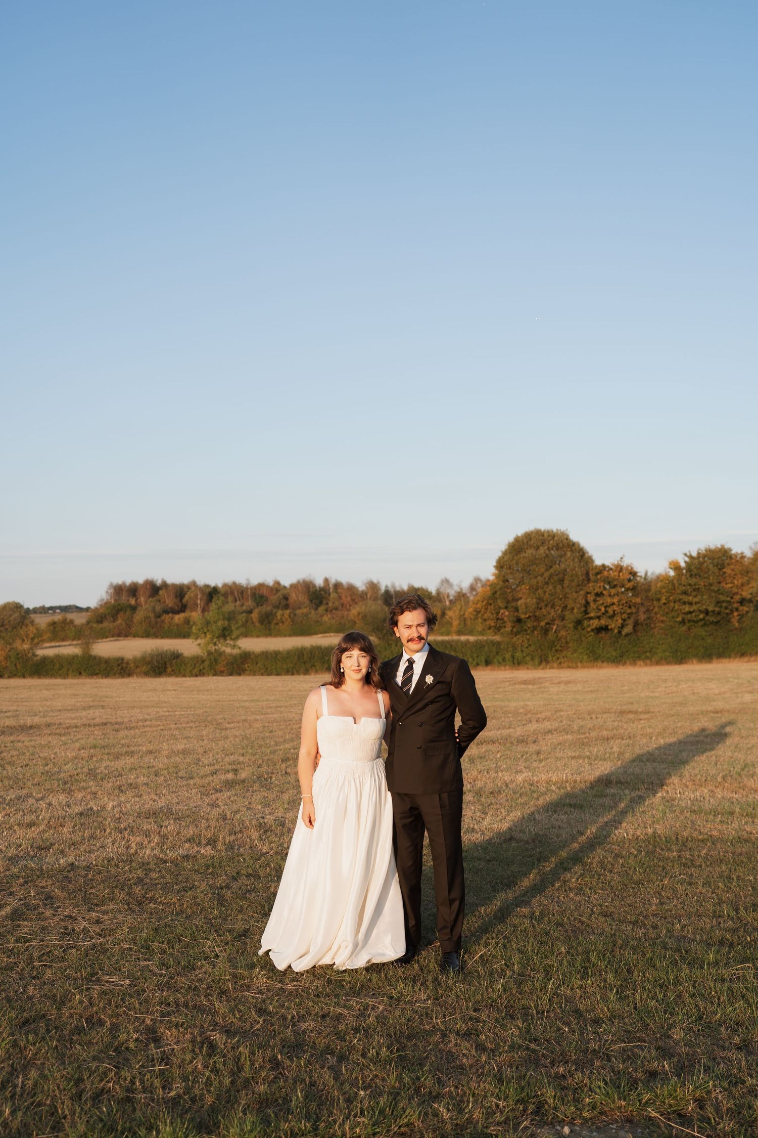 Couple walking together in an open field during golden hour.