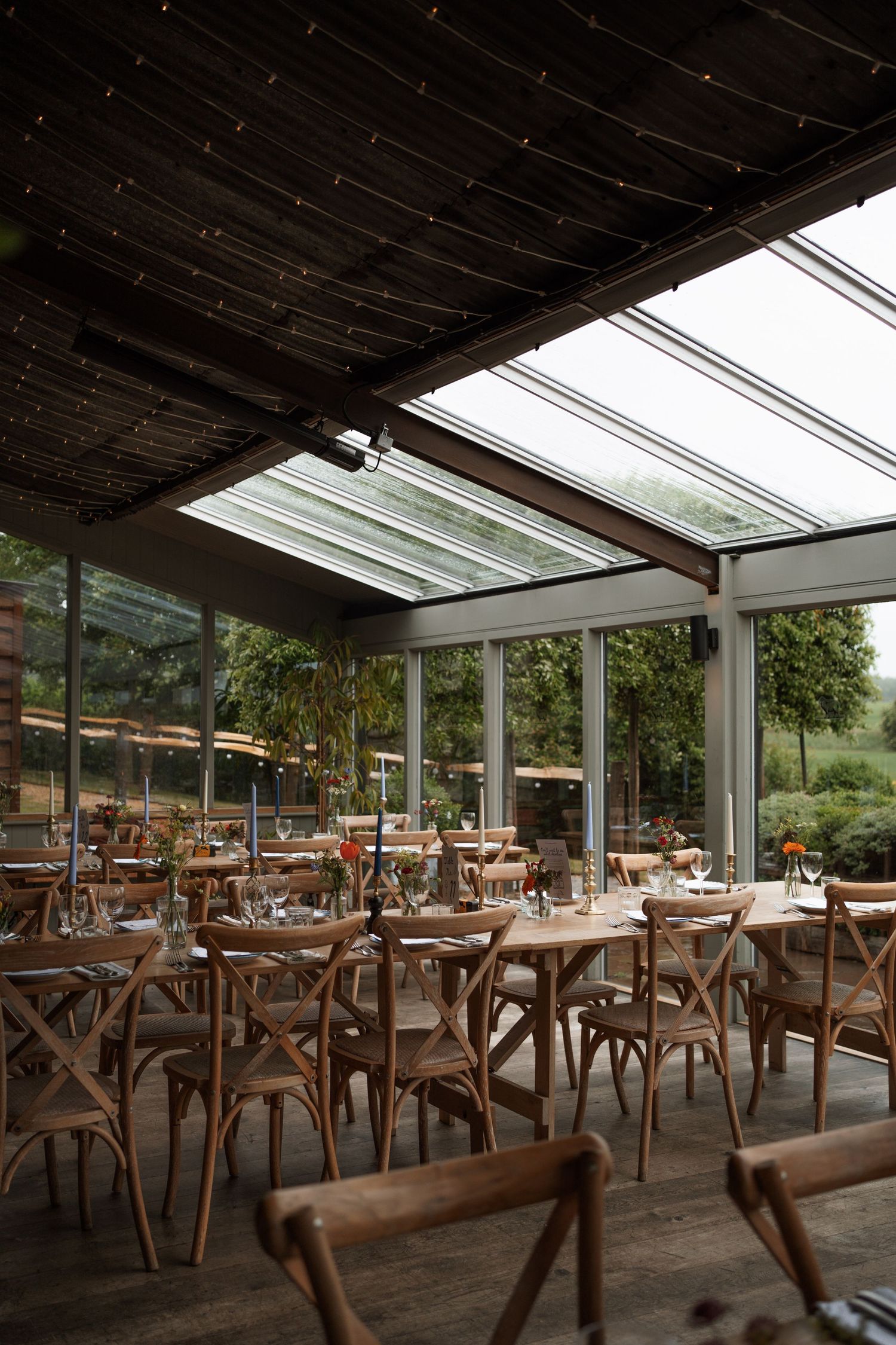 Rustic restaurant interior with wooden chairs and glass ceiling letting in natural light.