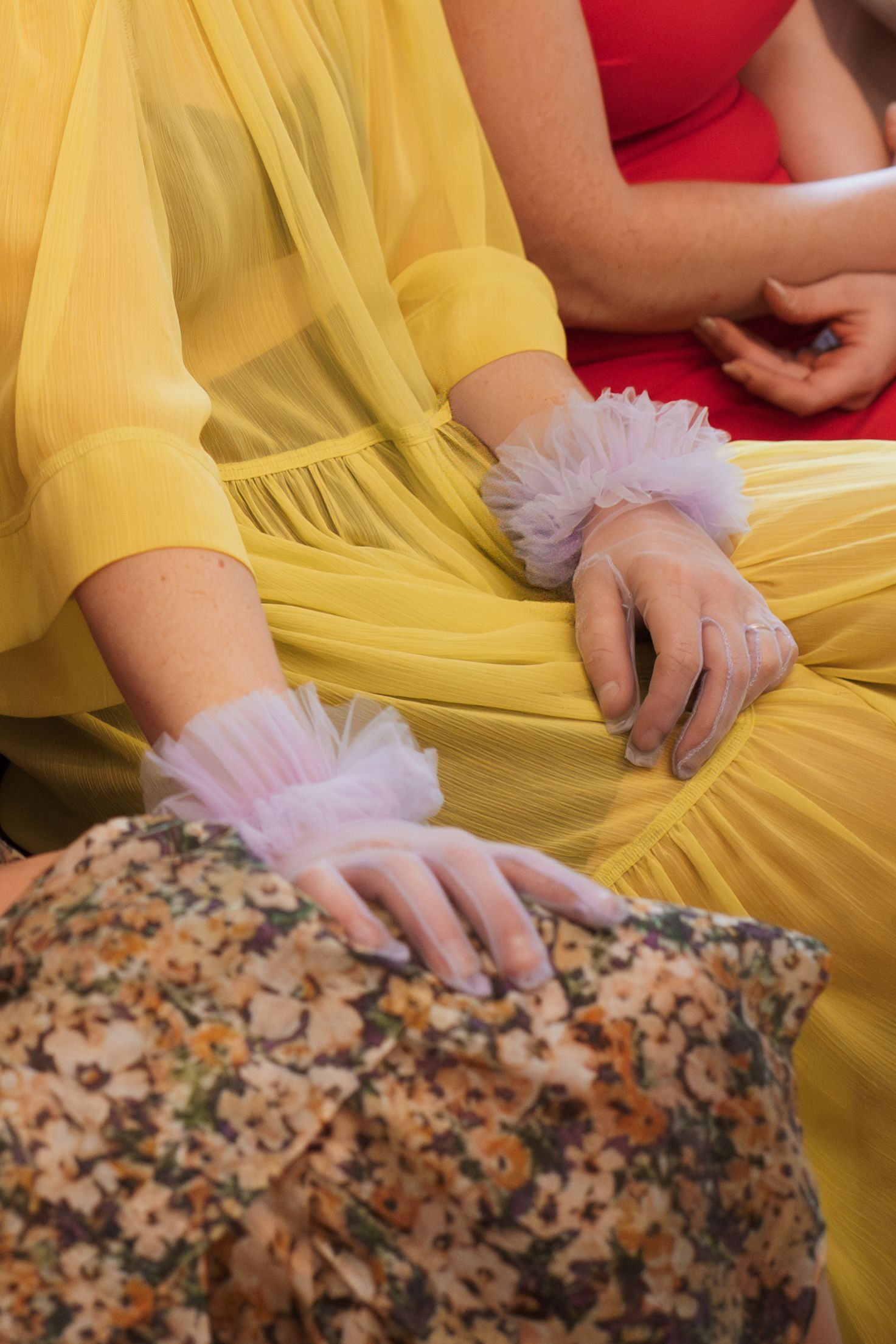 Person in yellow dress with tulle gloves resting hands on a patterned surface.