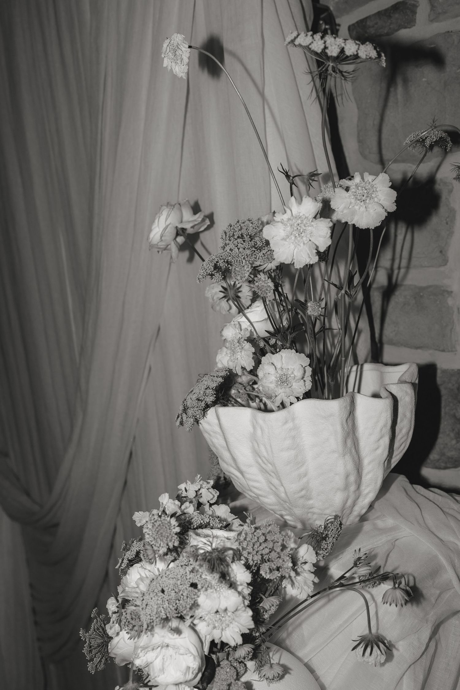 Artistic black and white shot of floral arrangements against draped fabric.