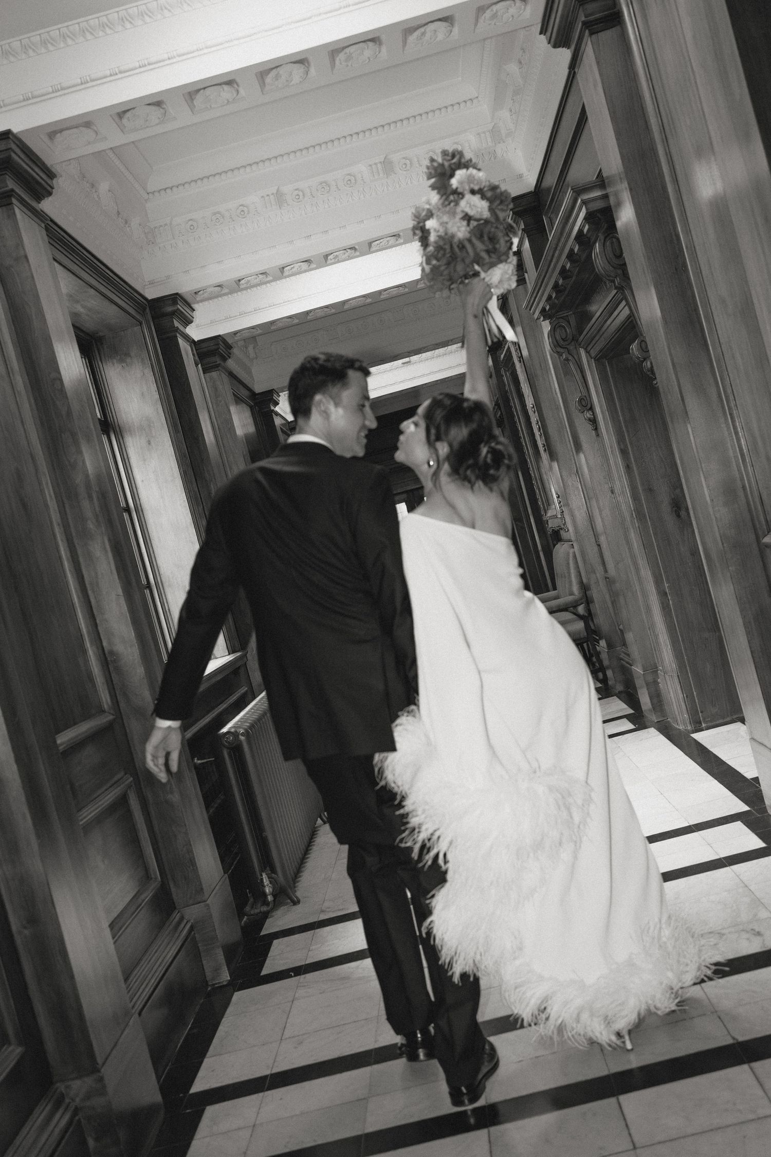 Wedding couple walking through an elegant hallway with white ornate ceiling.