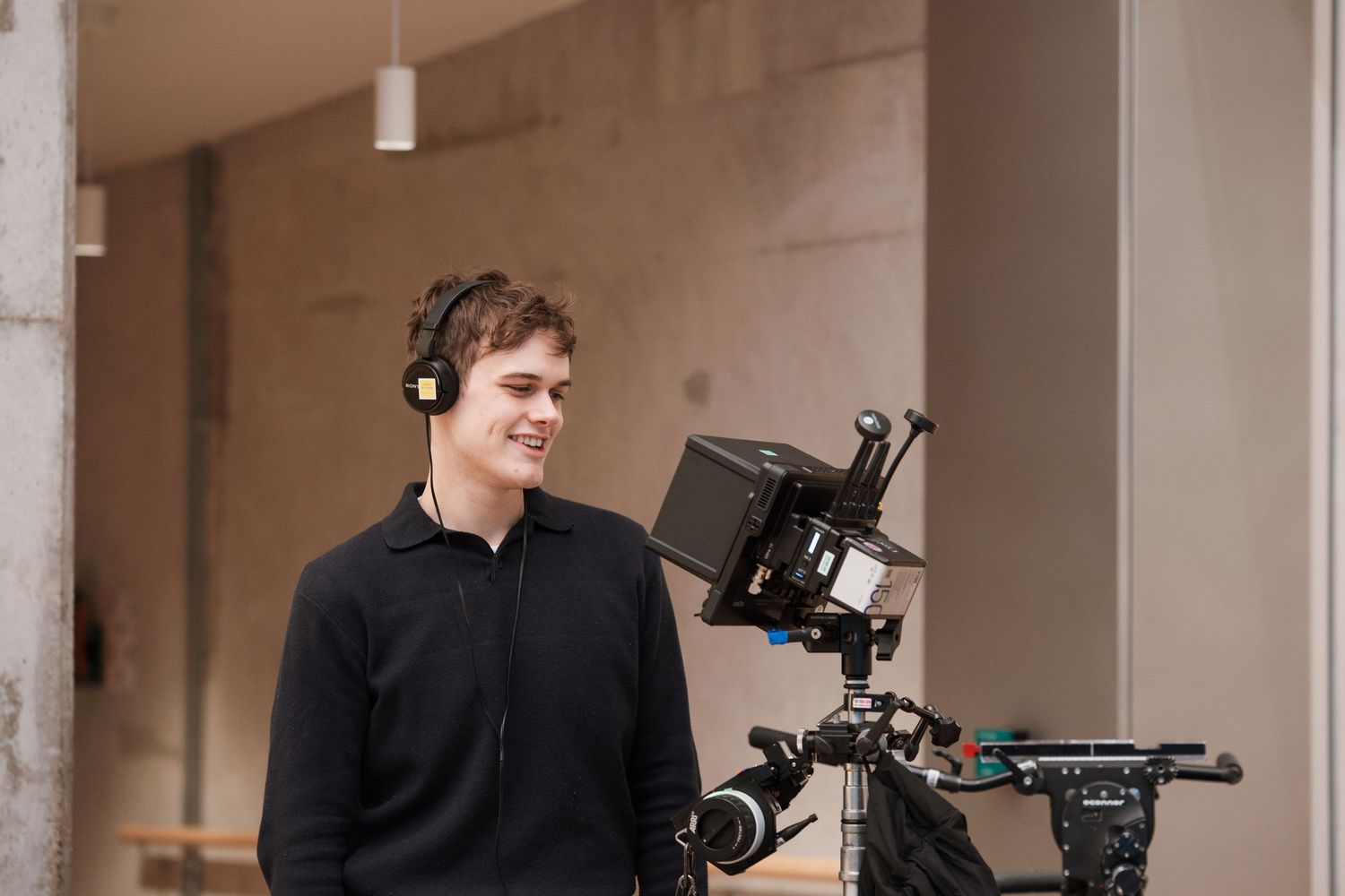 Smiling young filmmaker wearing headphones operating a professional camera rig on a film set.