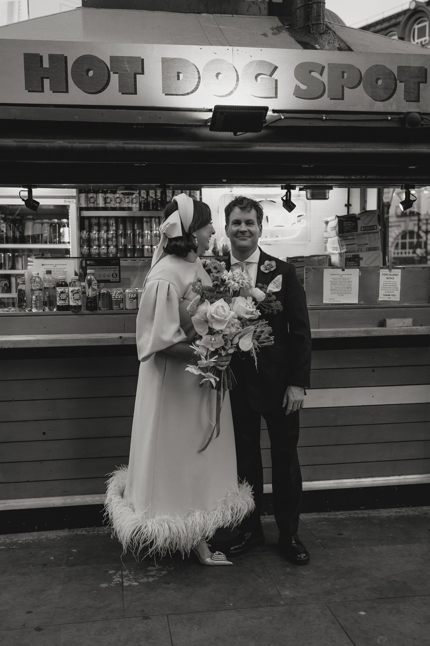 Wedding couple poses outside Hot Dog Spot restaurant in vintage black and white photo.