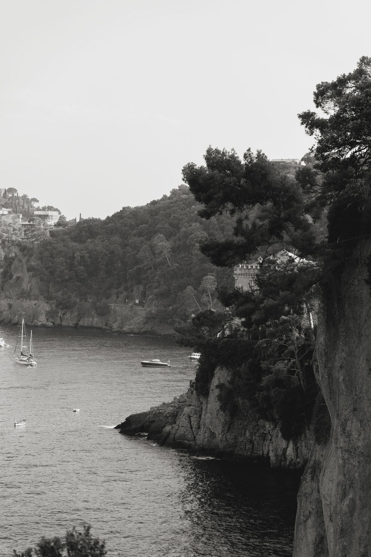 Black and white coastal landscape with cliffs and boats in a serene bay.