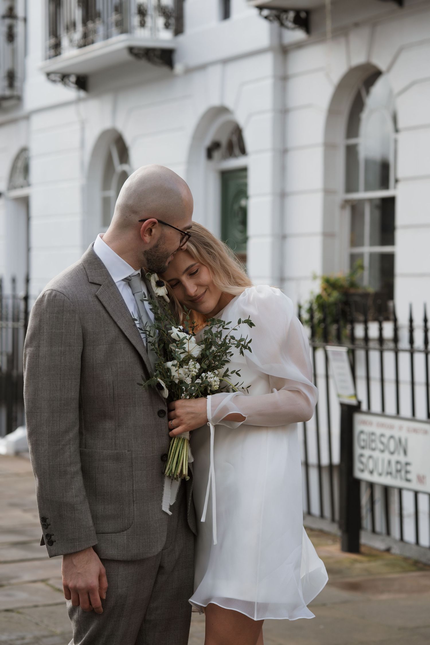 Romantic wedding couple posing against white Georgian architecture with iron railings.