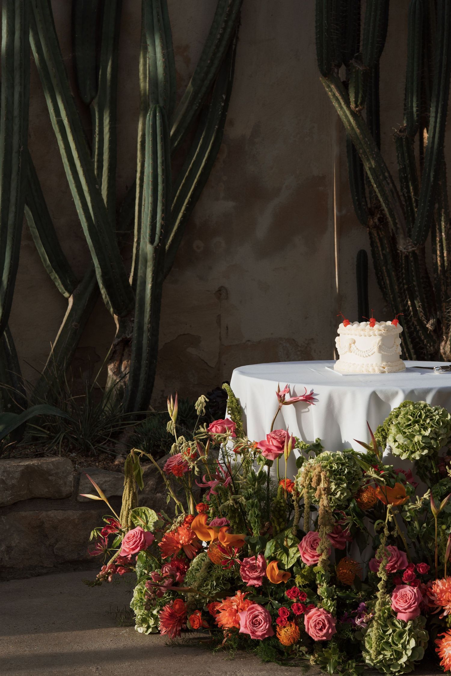 Lush floral arrangements with coral and pink roses line a white-clothed table against tropical plants.