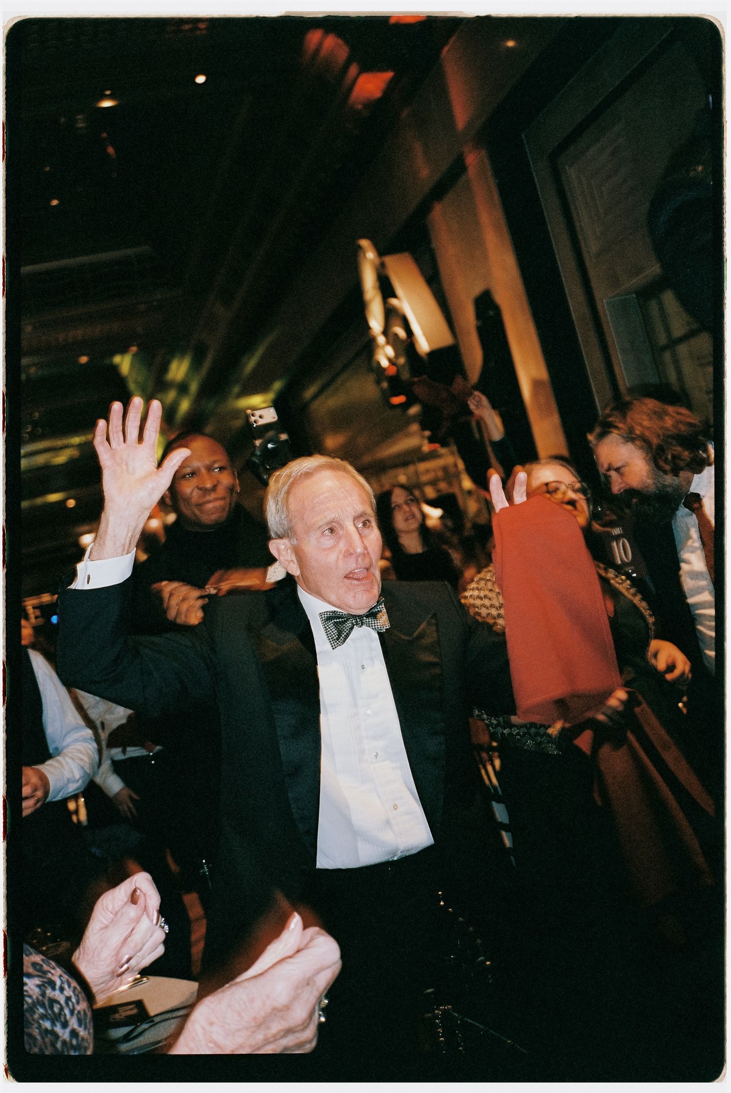 Guest in black tie attire raising hands in celebration at an evening event.