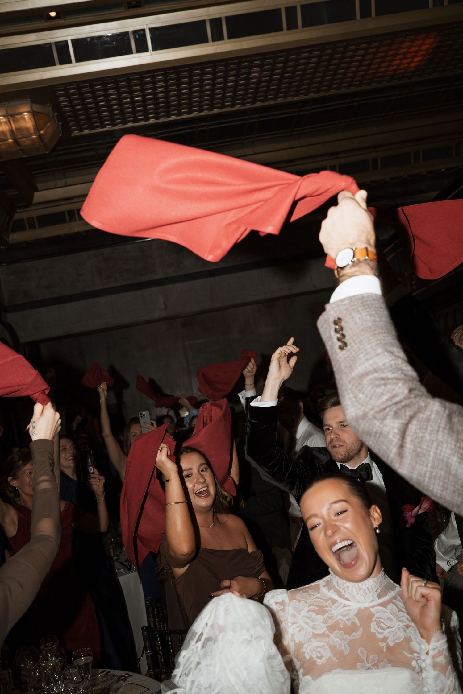Wedding celebration with crowd waving red napkins and dancing enthusiastically at a lively reception party.