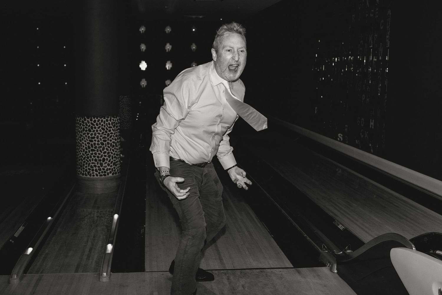 Someone mid-throw during a bowling game in a dark alley setting.