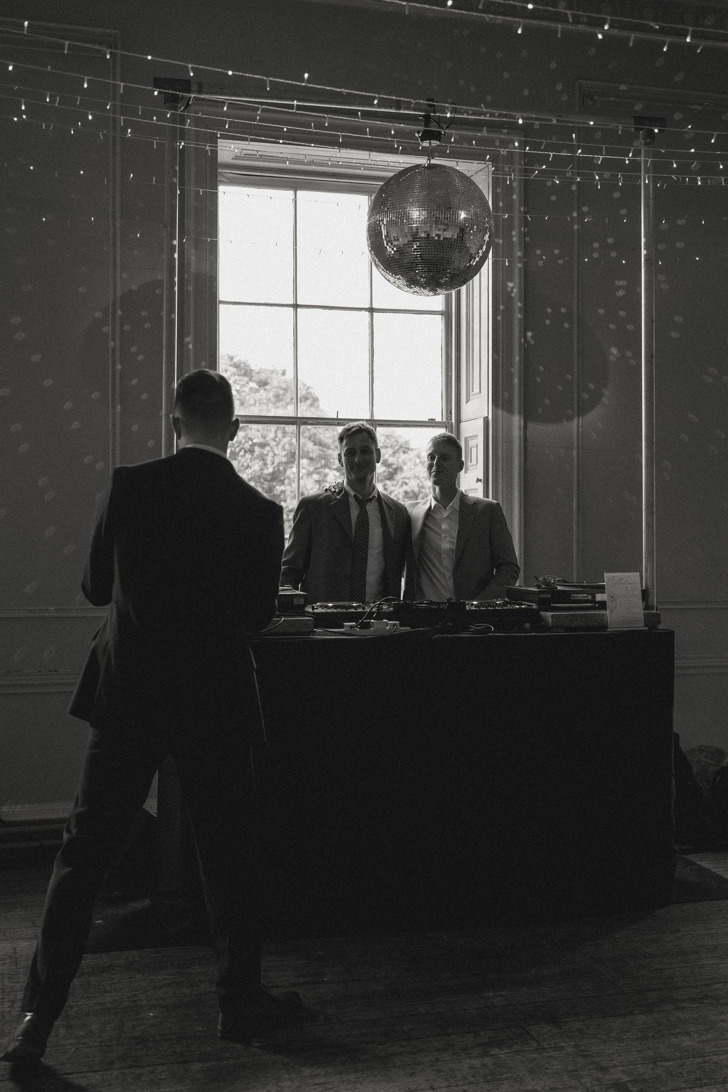 Dark reception hall with string lights and silhouettes of guests near buffet tables.