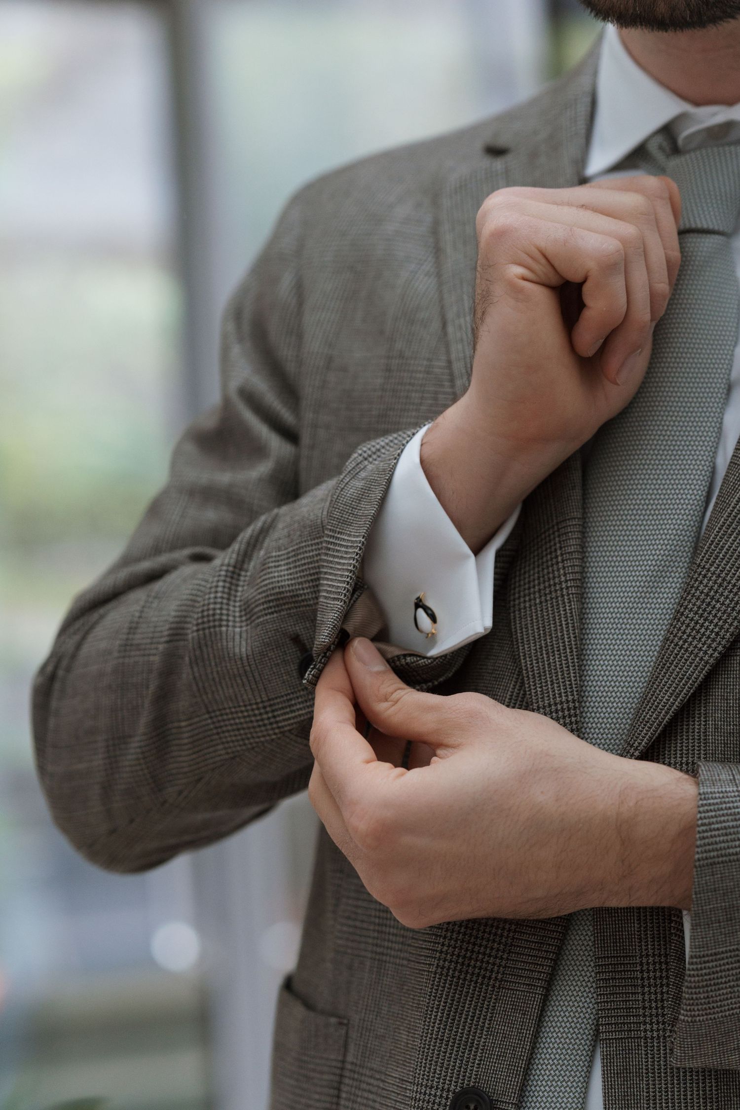 Close-up shots of hands adjusting the sleeve and cuff of a gray plaid suit jacket.