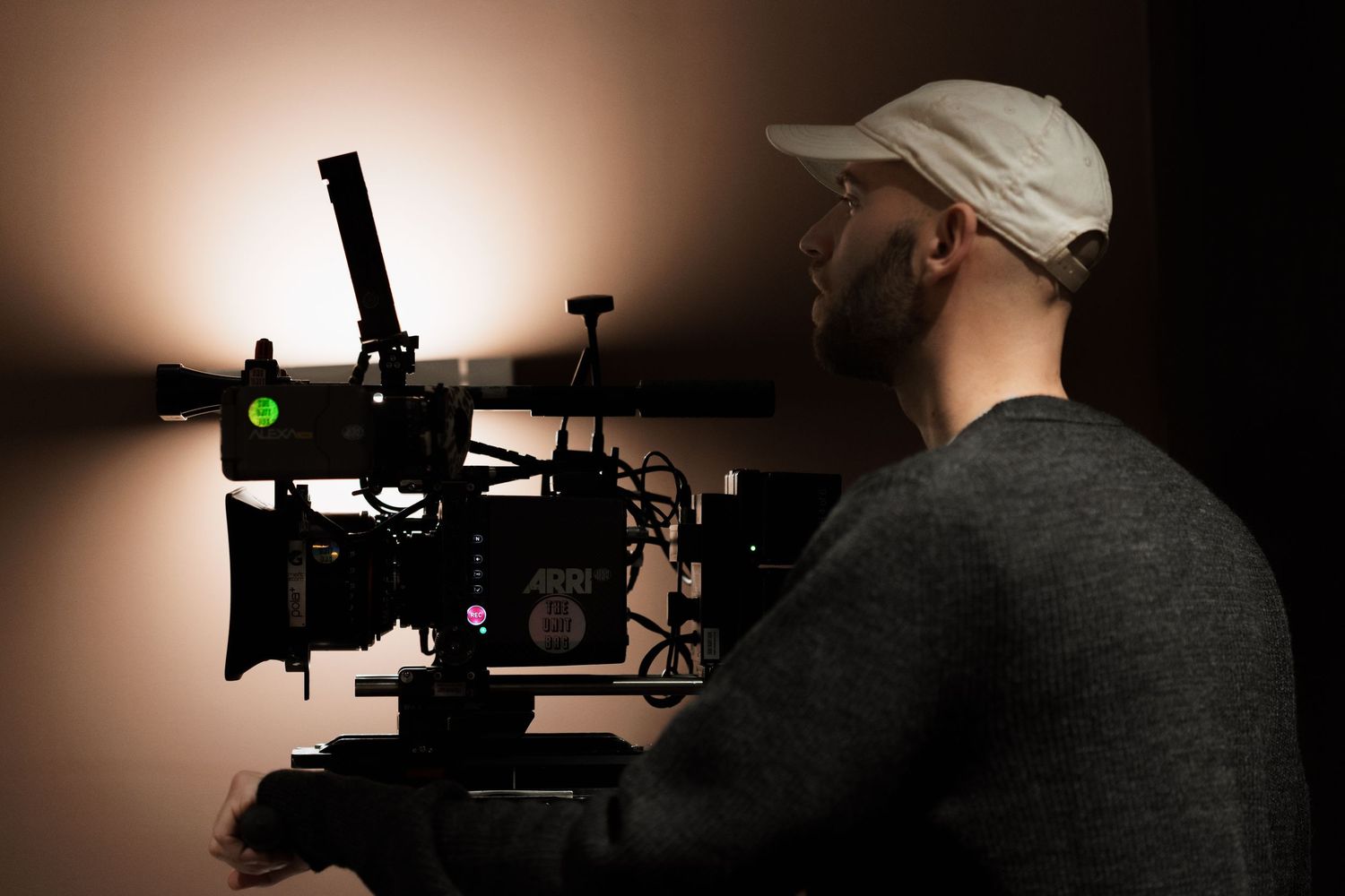 Cinematographer operating a professional cinema camera on a dark film set with warm background lighting.