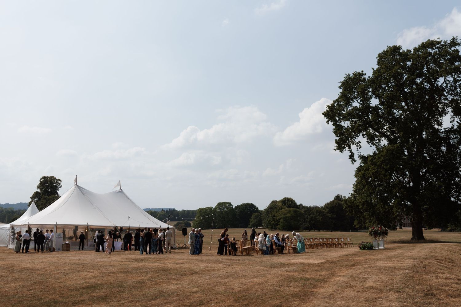 Panoramic view of white wedding tents set up in a sprawling field with trees in the distance.
