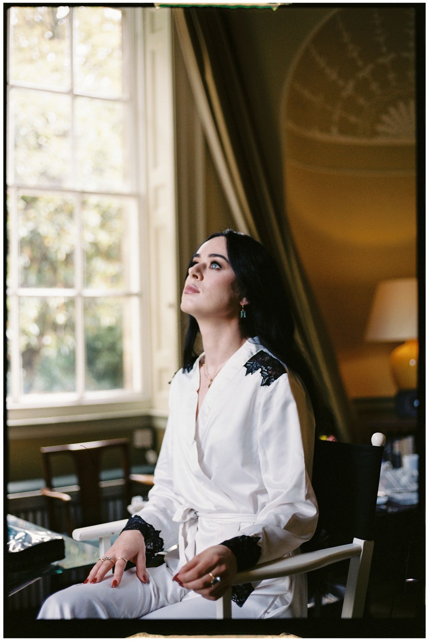 Person in white robe sitting by window in elegant room during morning preparation.