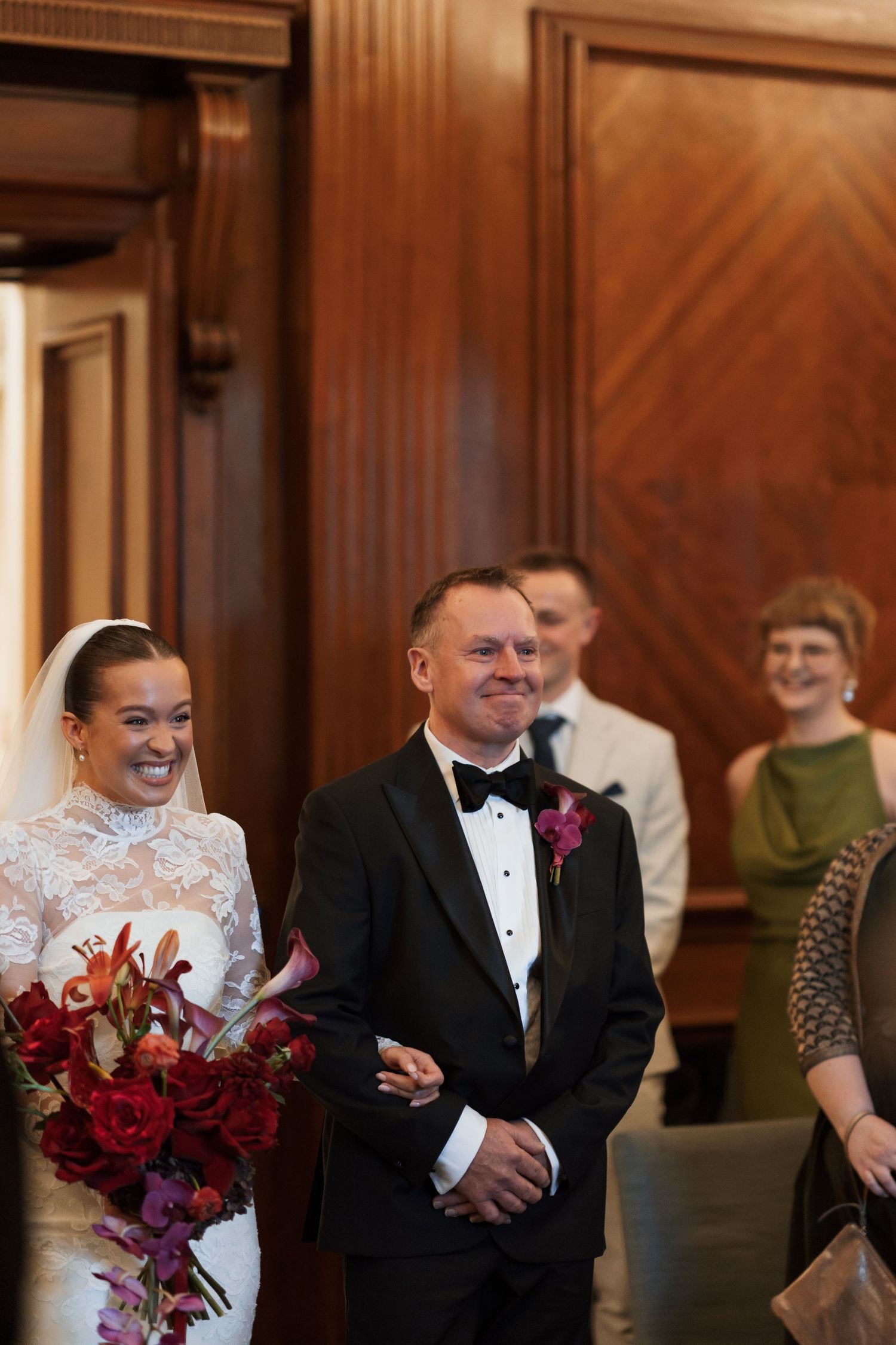 Wedding celebration in wood-paneled room with red floral bouquet.