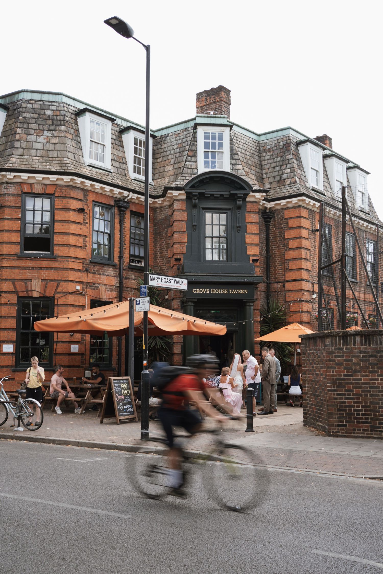 Historic brick building exterior with orange awnings and cyclists passing by on the street.