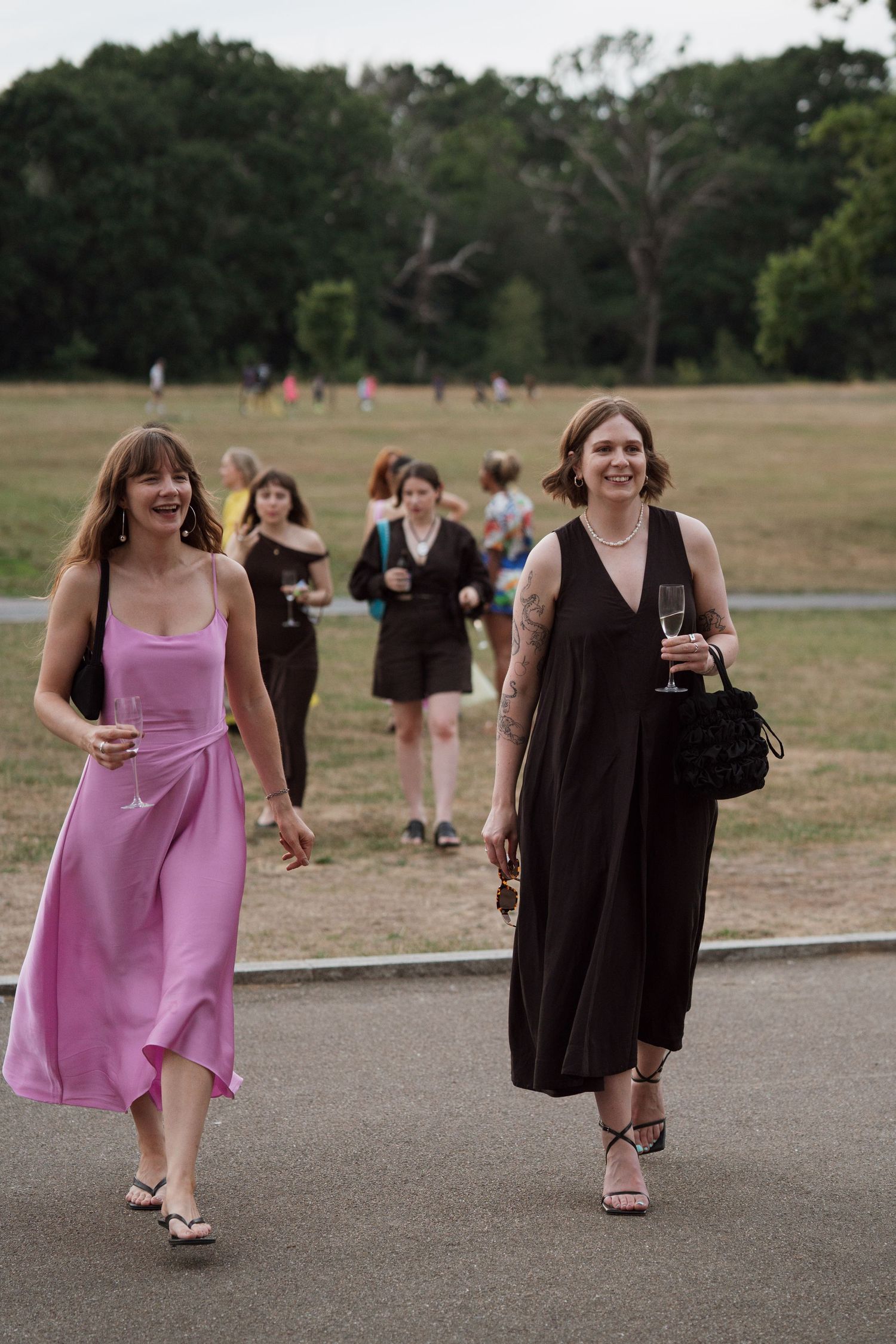 Wedding guests in pink and brown dresses walking along an outdoor path.