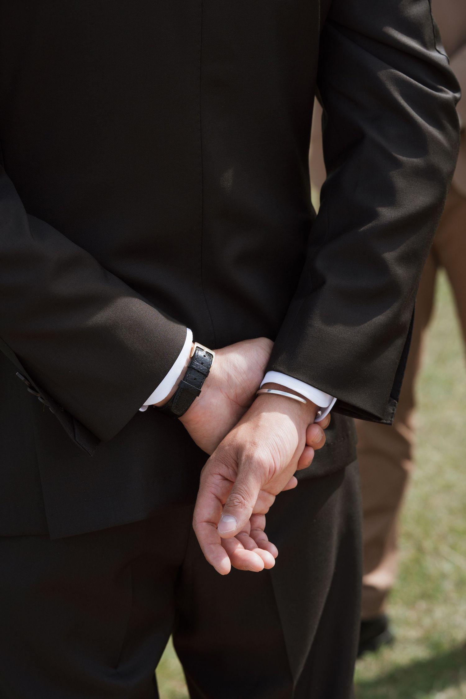 Close-up of hands in formal attire clasped behind someone's back.