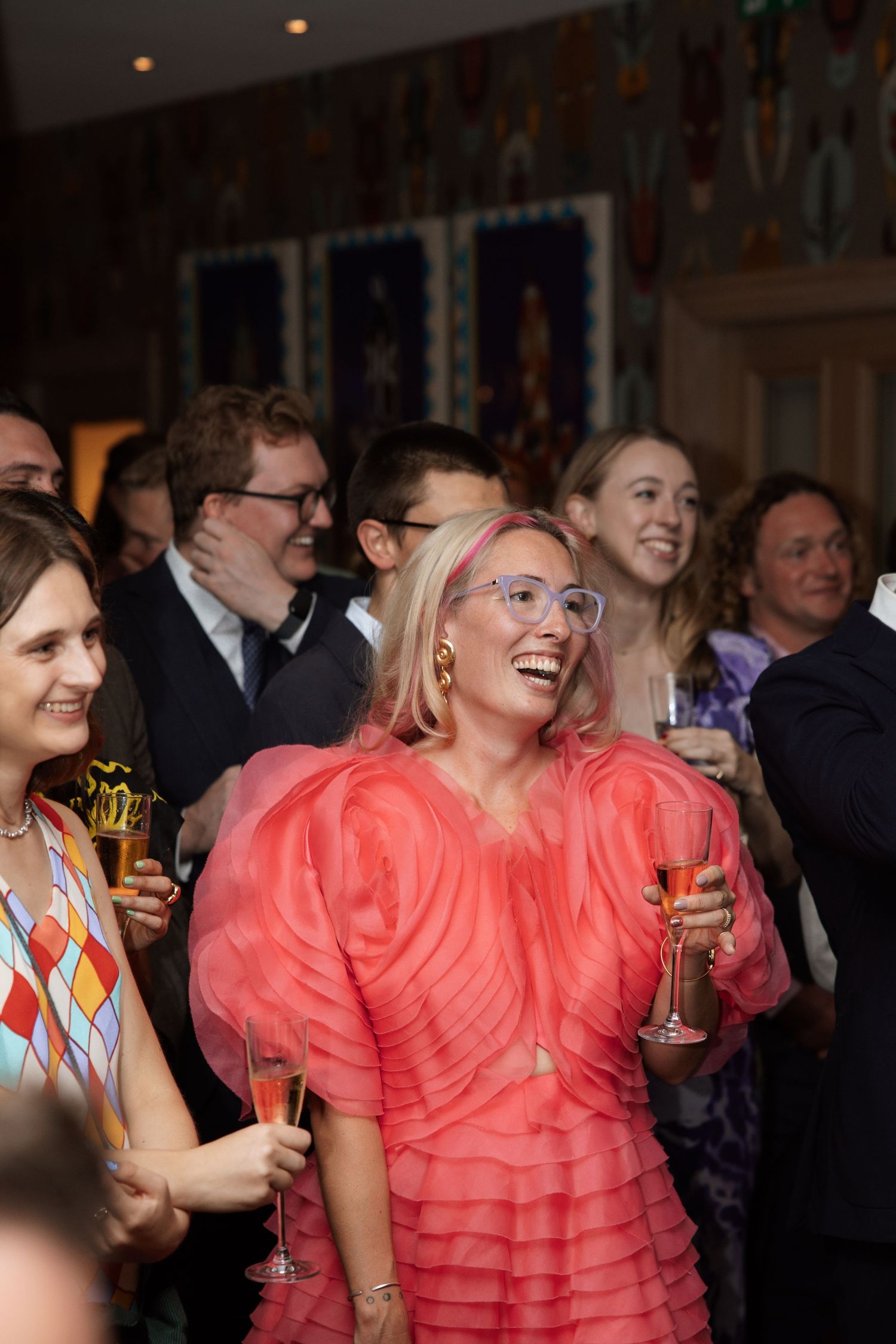 Group of party guests in coral dresses enjoying drinks at an evening celebration.
