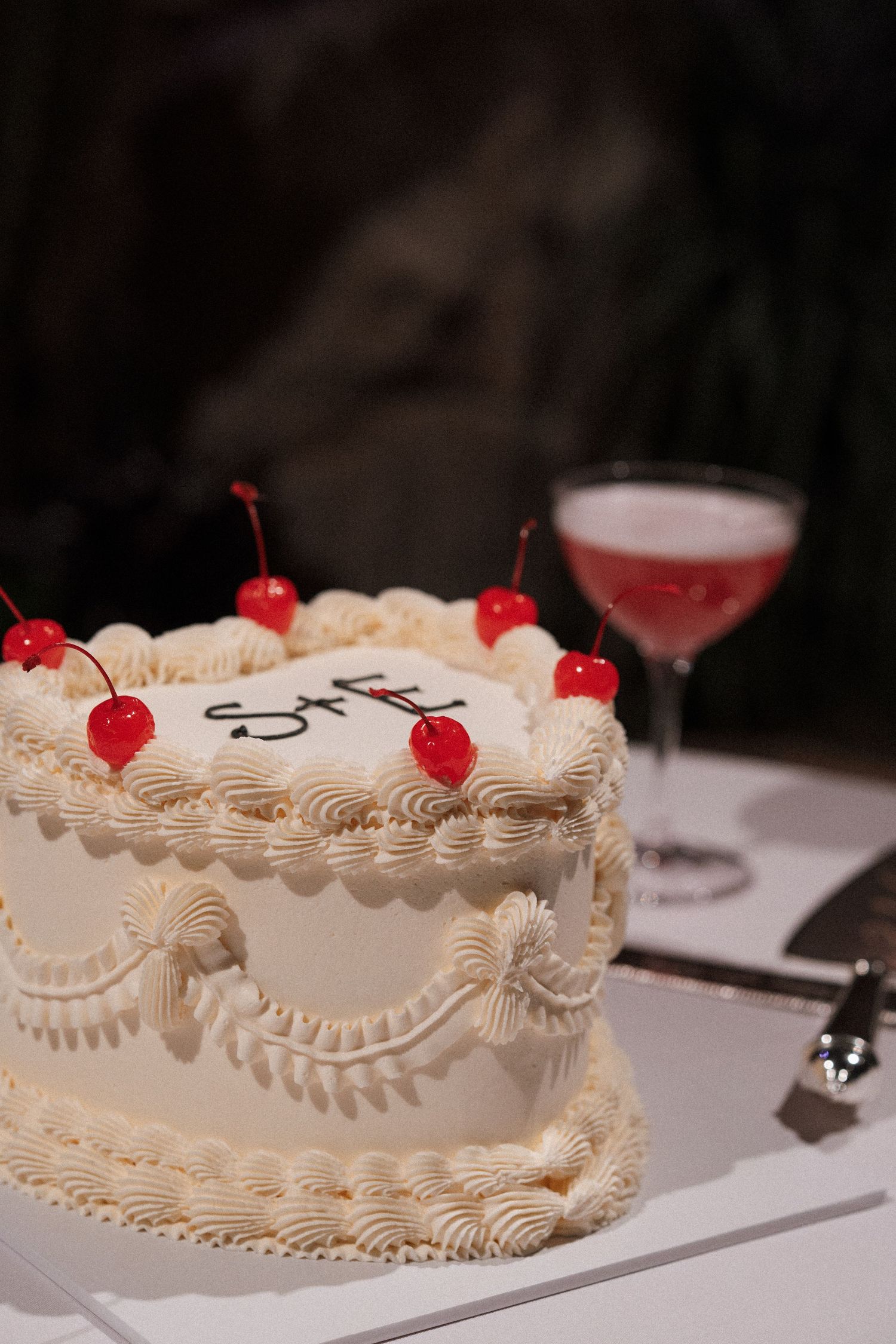 White wedding cake decorated with intricate piping and topped with red cherries.