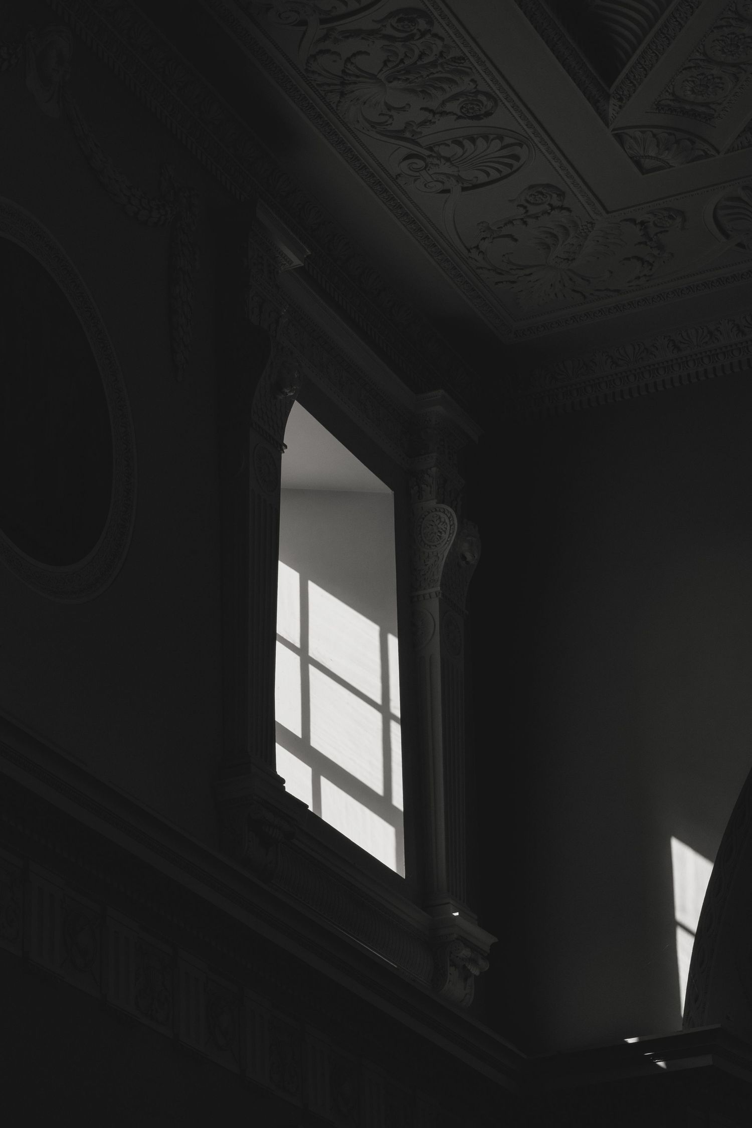 Dramatic light streams through windows in a dark room with ornate ceiling details.