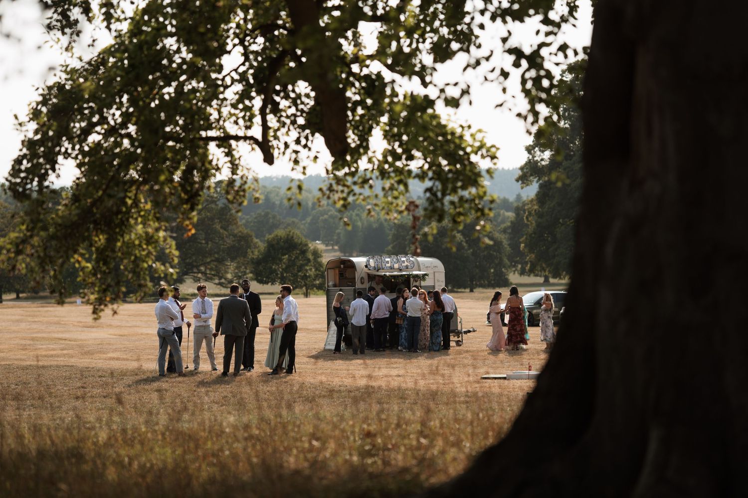 Silhouetted figures gathered under trees at sunset during an outdoor event.