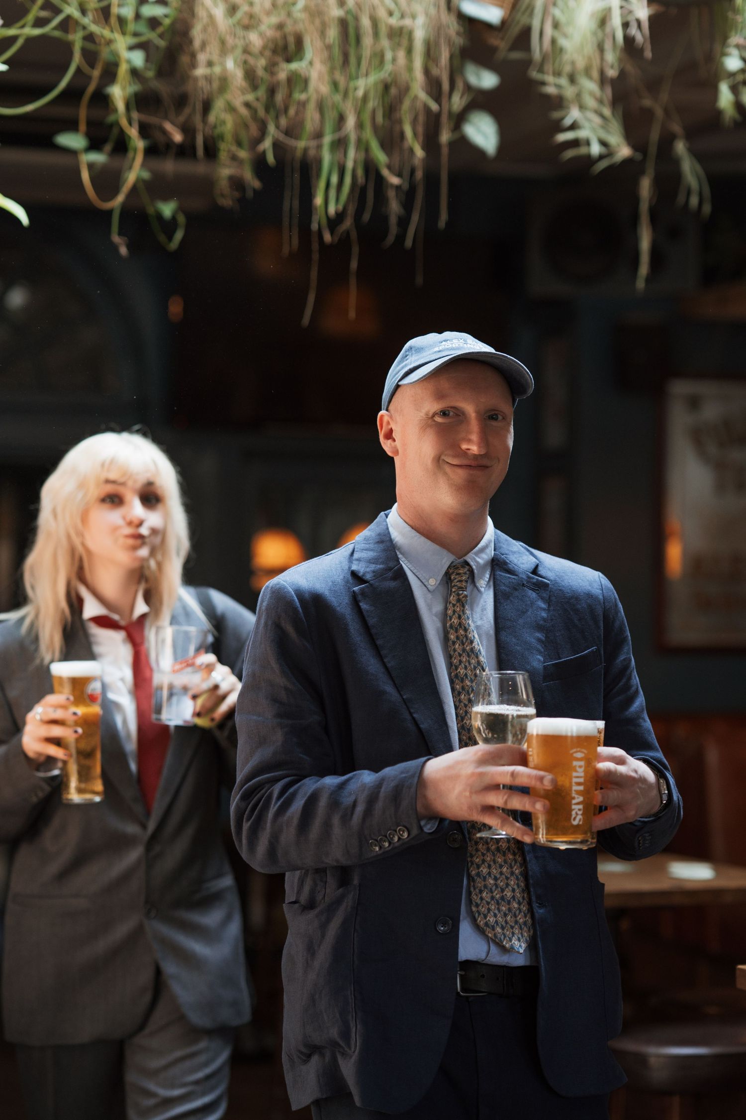 People enjoying beers at an indoor venue with hanging decorative plants.
