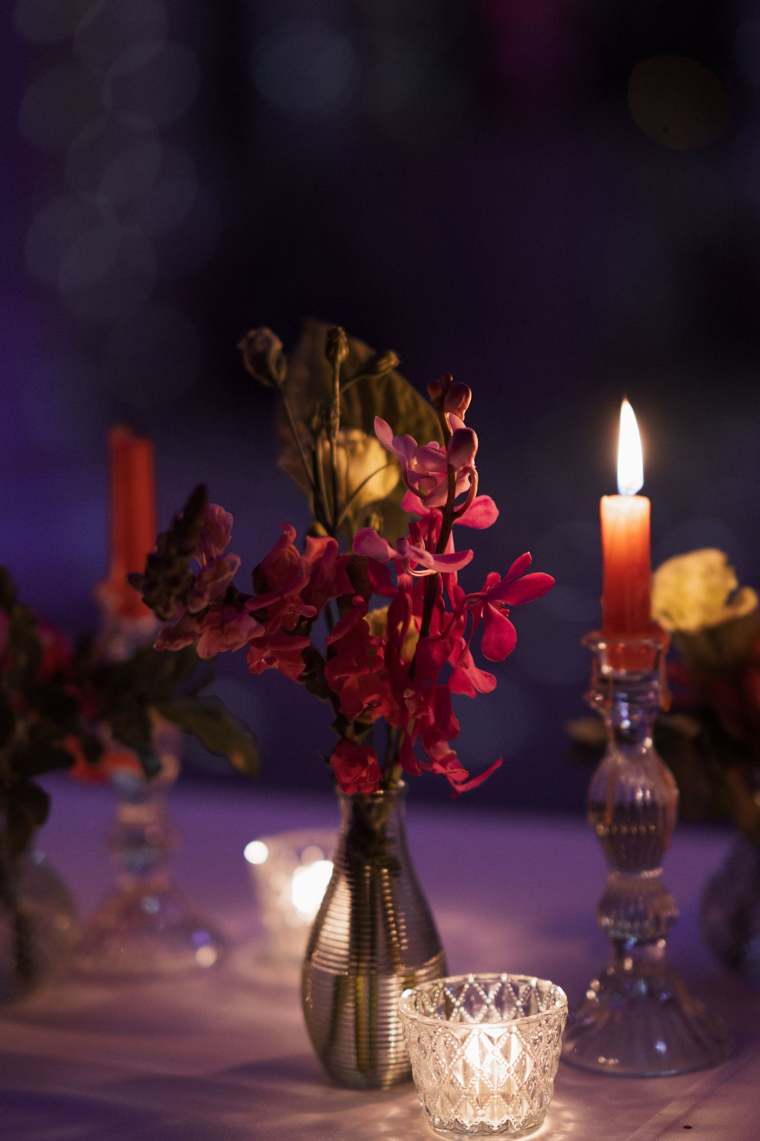 Moody evening table setting with red flowers in a vase and glowing candles.