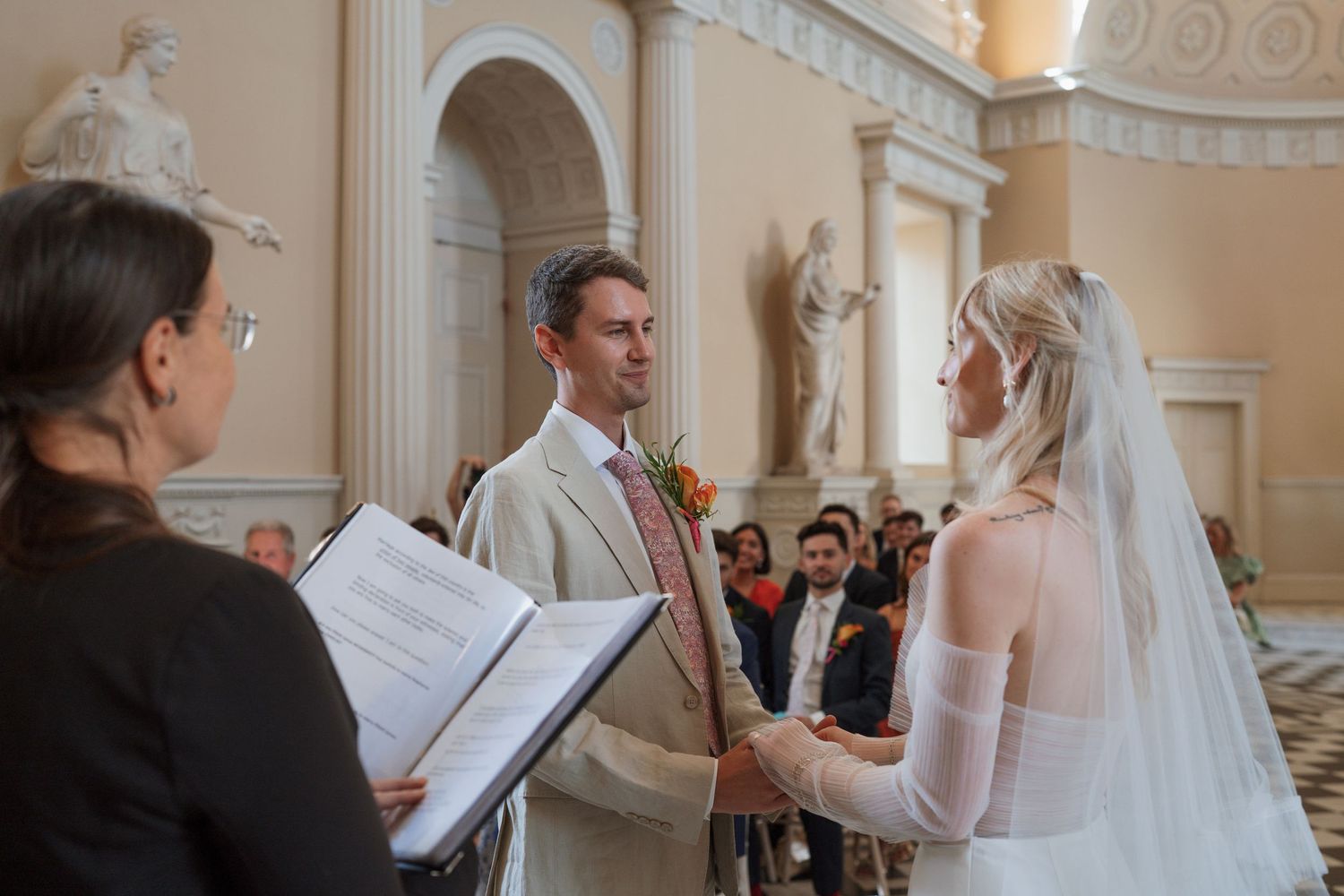 A wedding ceremony taking place in an elegant room with classical architecture and columns.