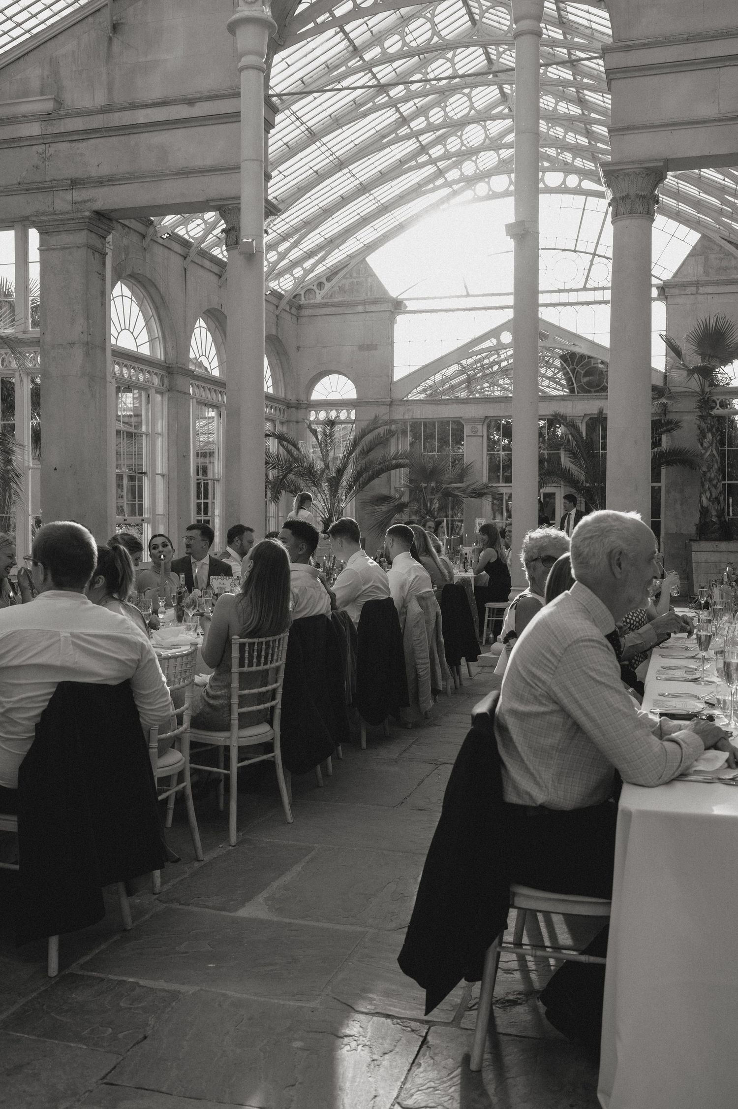 Black and white photo of wedding reception in a grand conservatory with glass ceiling.