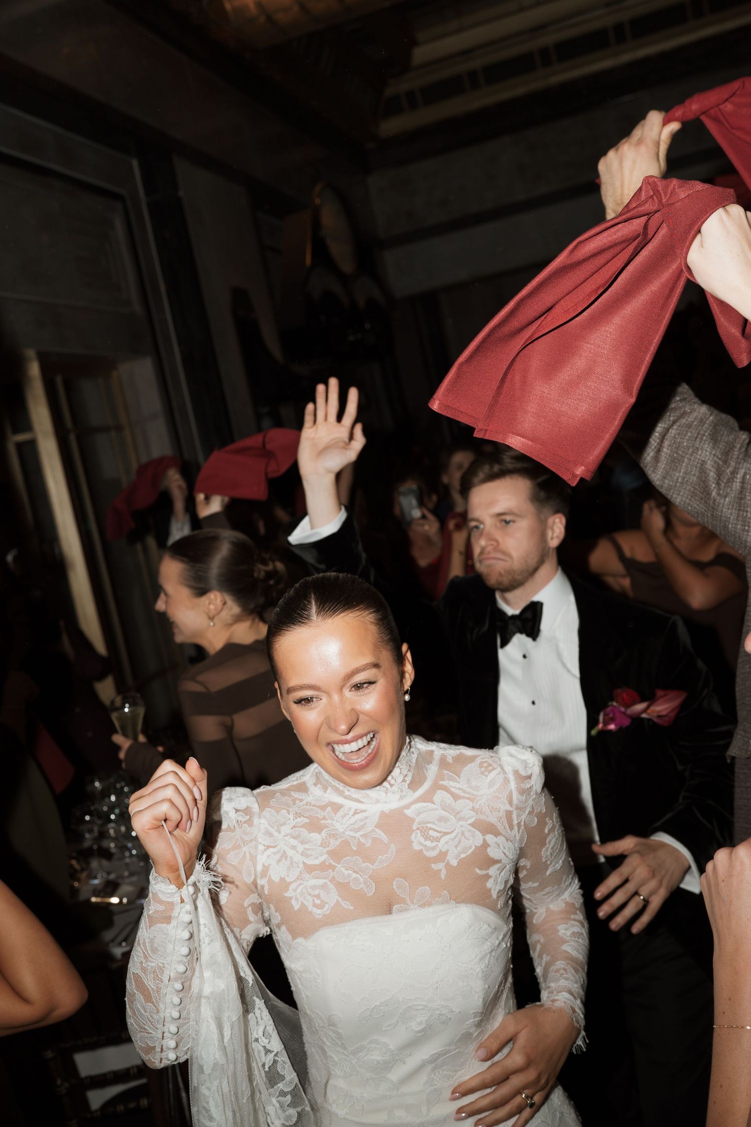 Lively wedding reception with guests waving red napkins while dancing and celebrating.