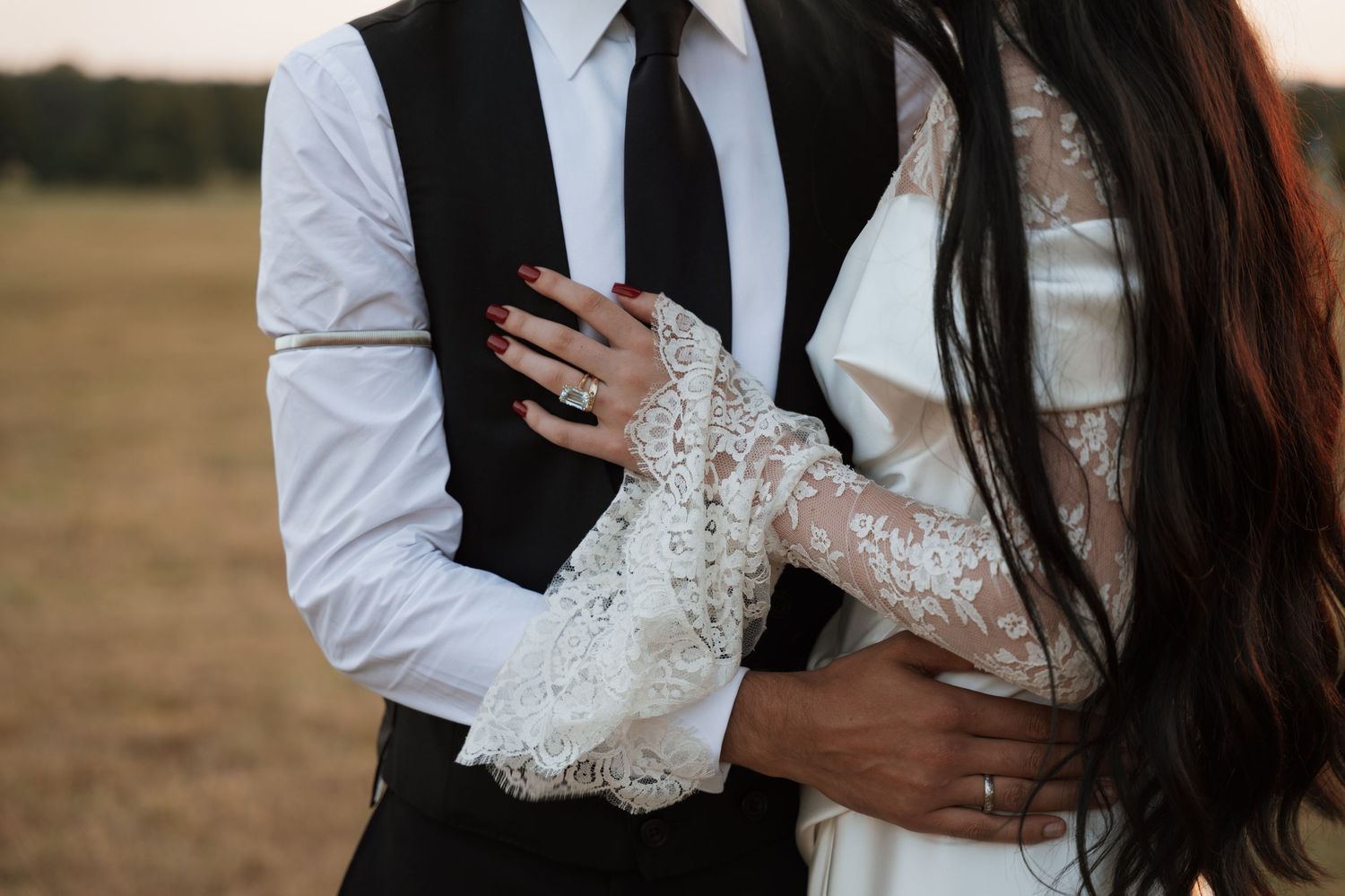 Close-up of wedding couple showing detailed lace sleeves and formal attire during sunset.