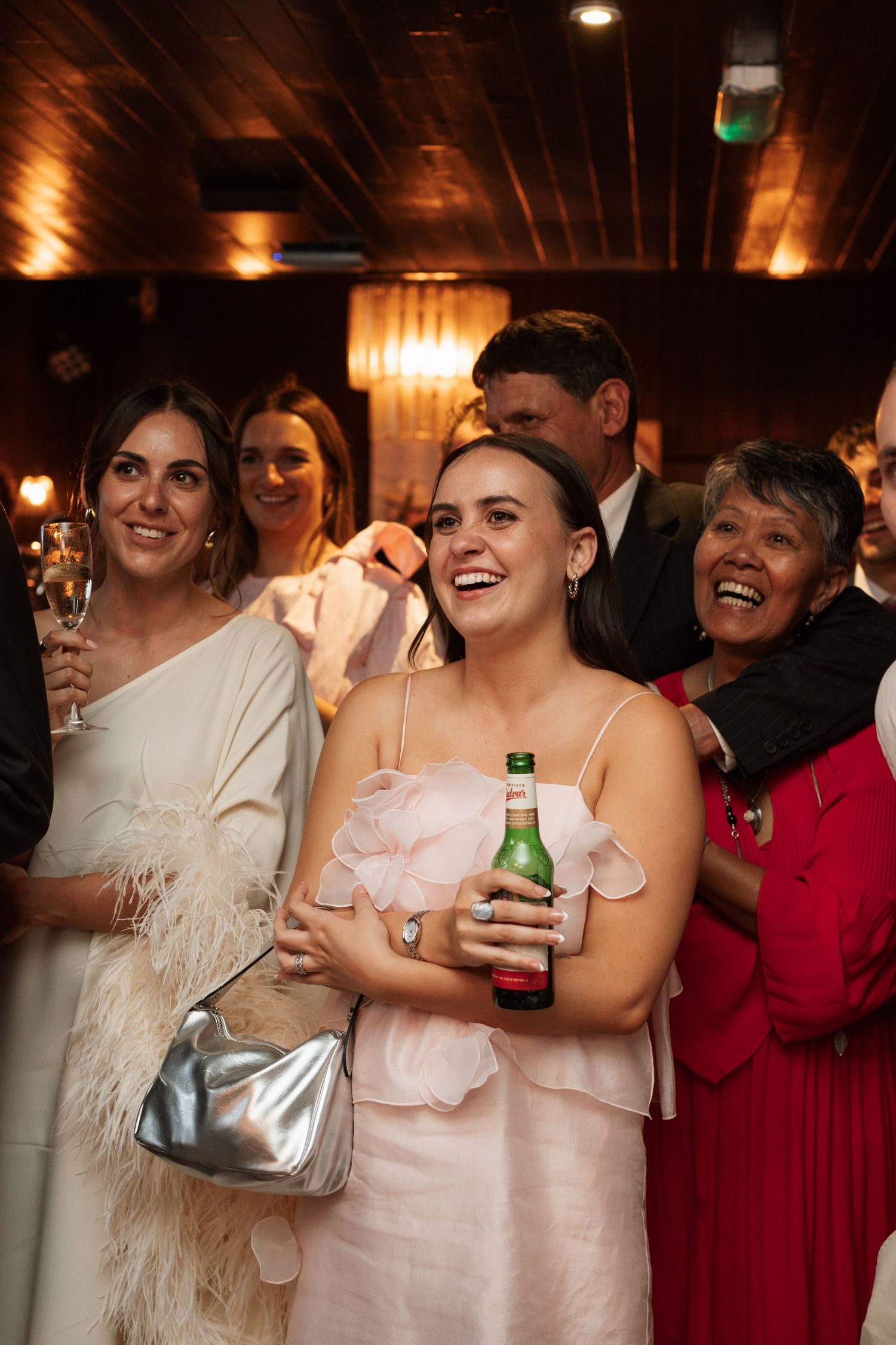 Wedding guests in formal attire laugh and celebrate at an indoor reception.