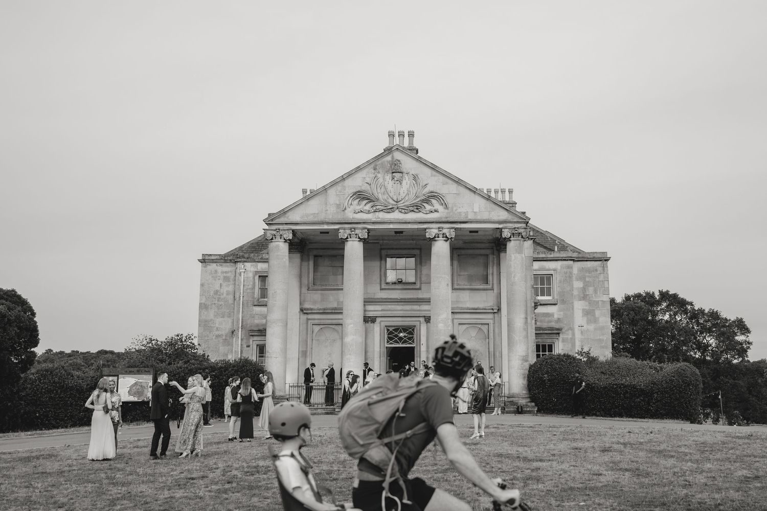 Classical architecture building exterior with columns and guests gathering on the lawn.