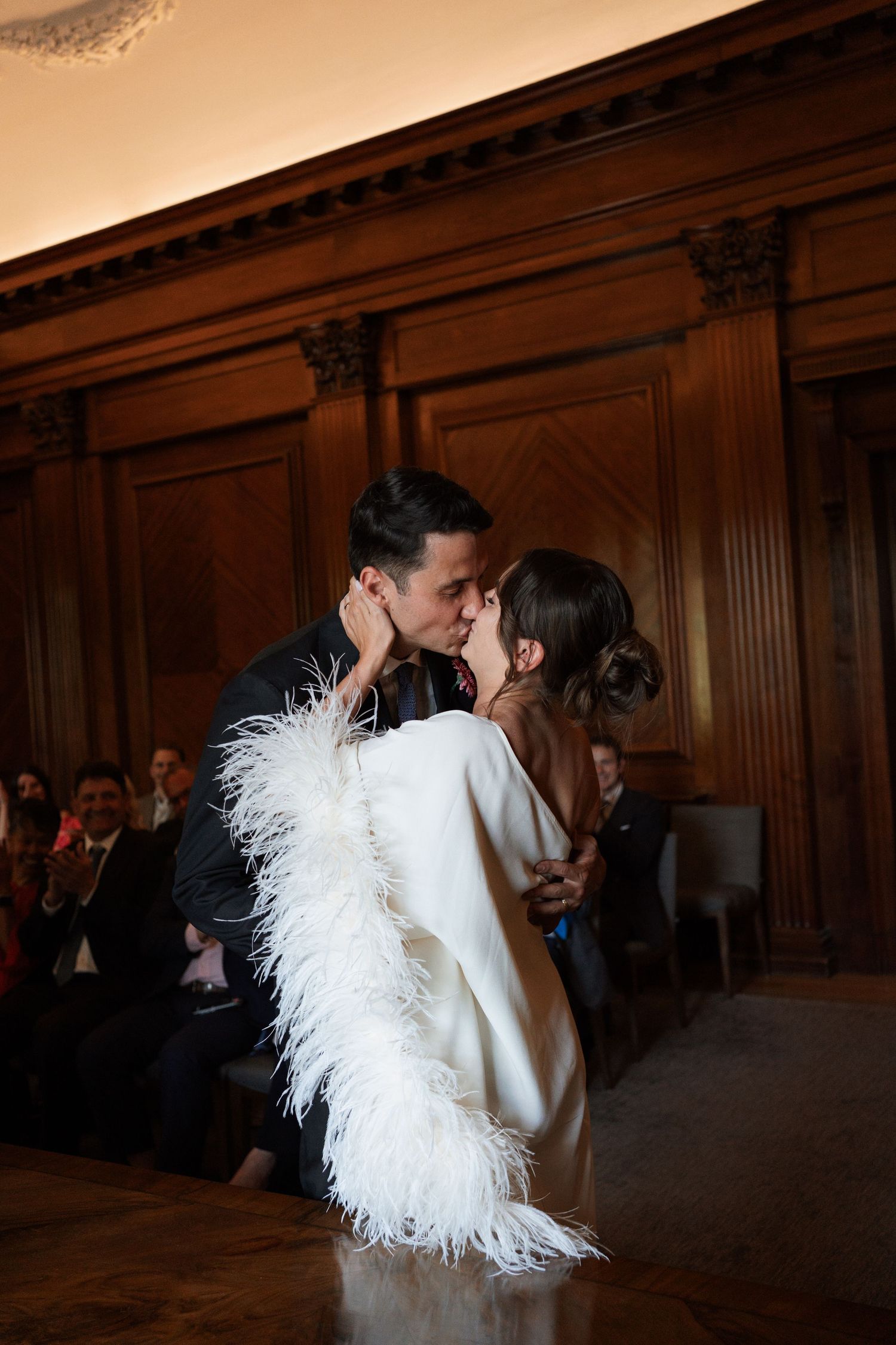 Romantic moment captured in wood-paneled venue with feathered dress detail.