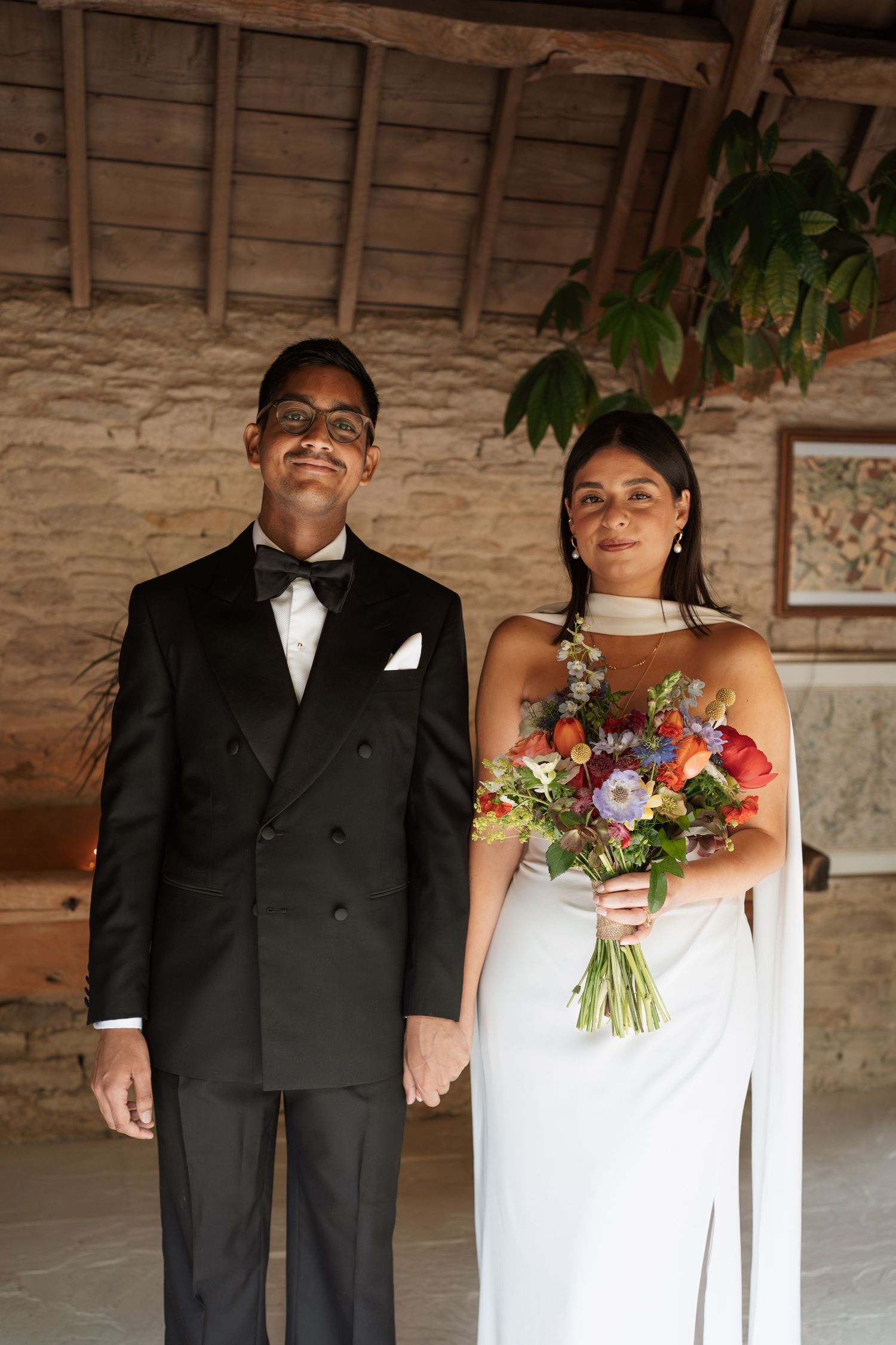 Wedding couple in formal attire holding hands in rustic stone building.