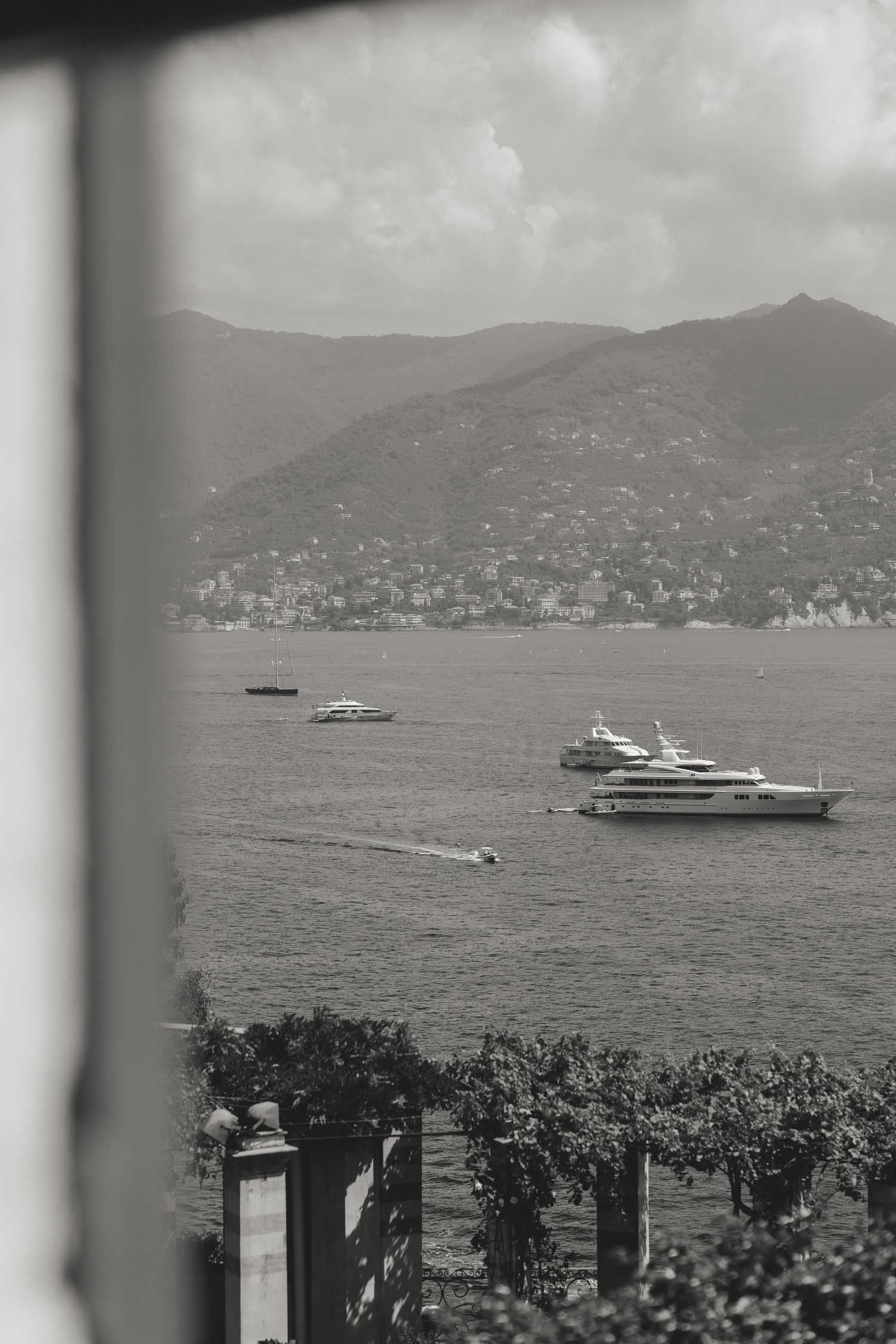 Luxury yachts anchored in a scenic bay with mountains and coastal buildings in the background.
