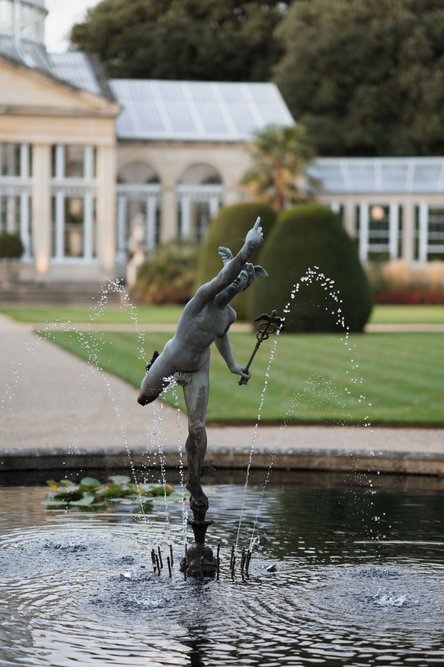 Bronze fountain statue spouts water in a decorative garden pond.