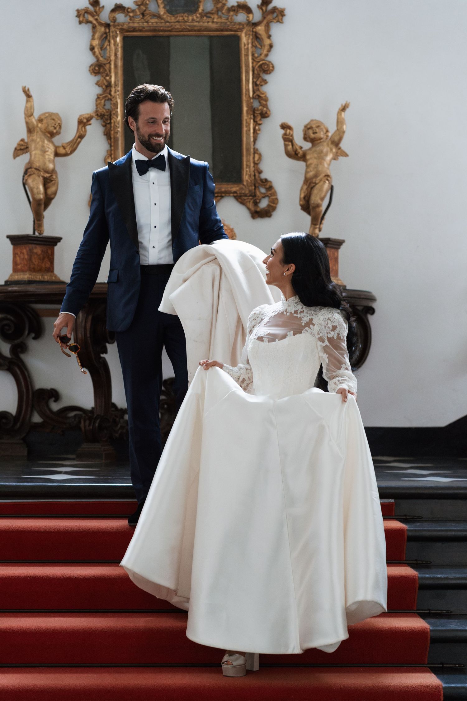 Elegant wedding scene showing couple dancing in formal attire against ornate baroque interior with gold frames.